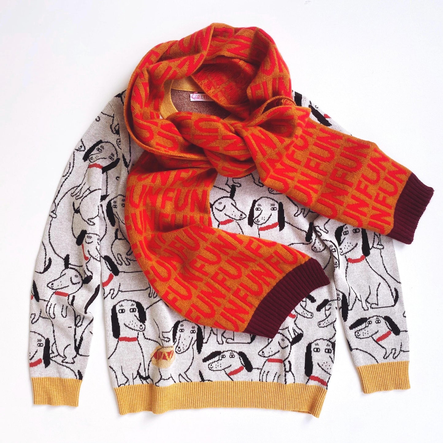 Orange patterned knitted scarf draped over a white sweater with dachshund dog design on a white background