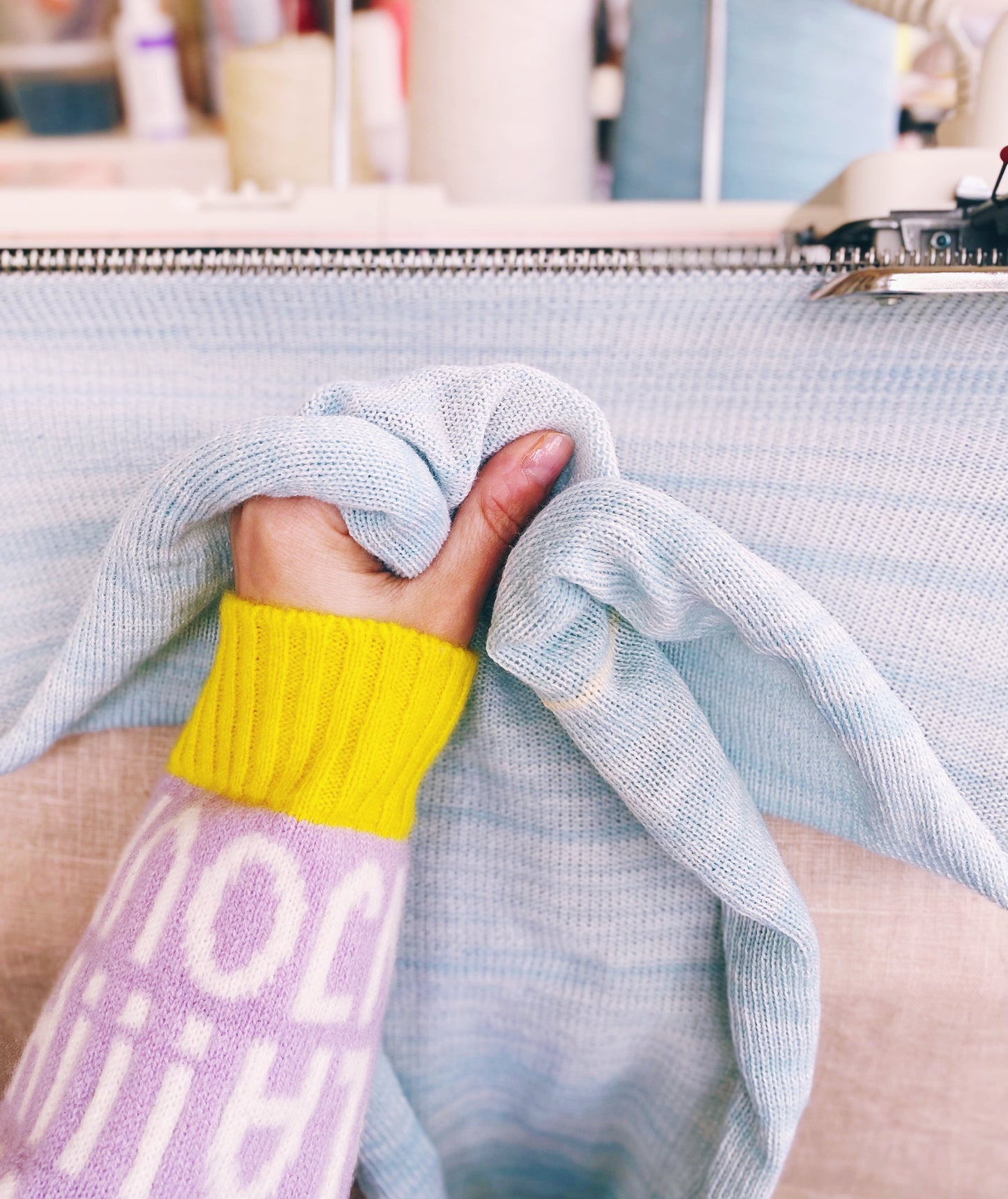 Person holding a light blue sweater with a blurred indoor background