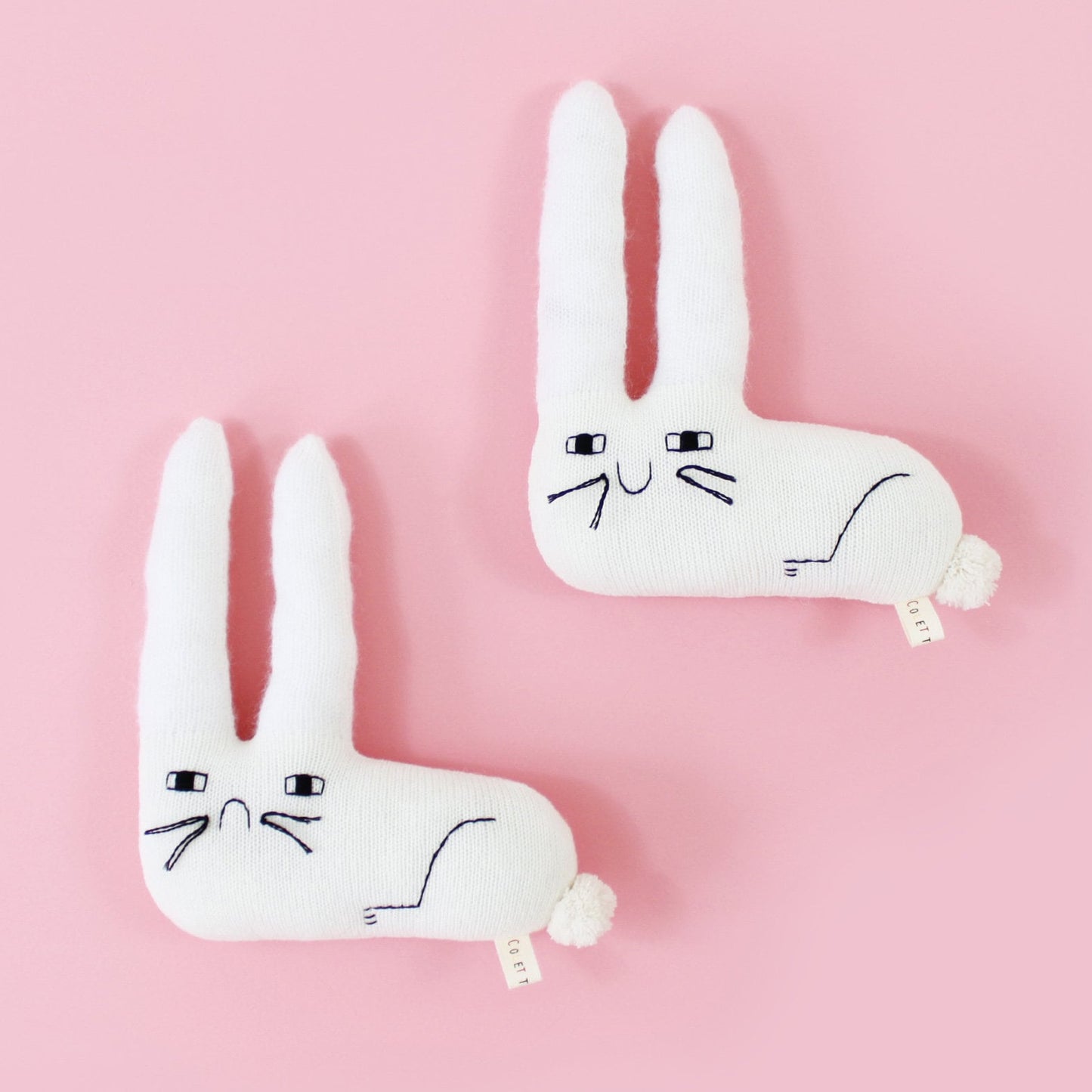 Two white rabbit knitted plush toys, one sad, one happy, on a pink background