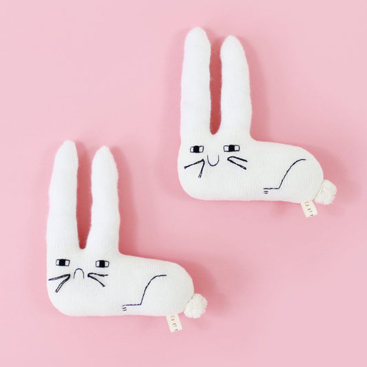 Two white rabbit knitted plush toys, one sad, one happy, on a pink background