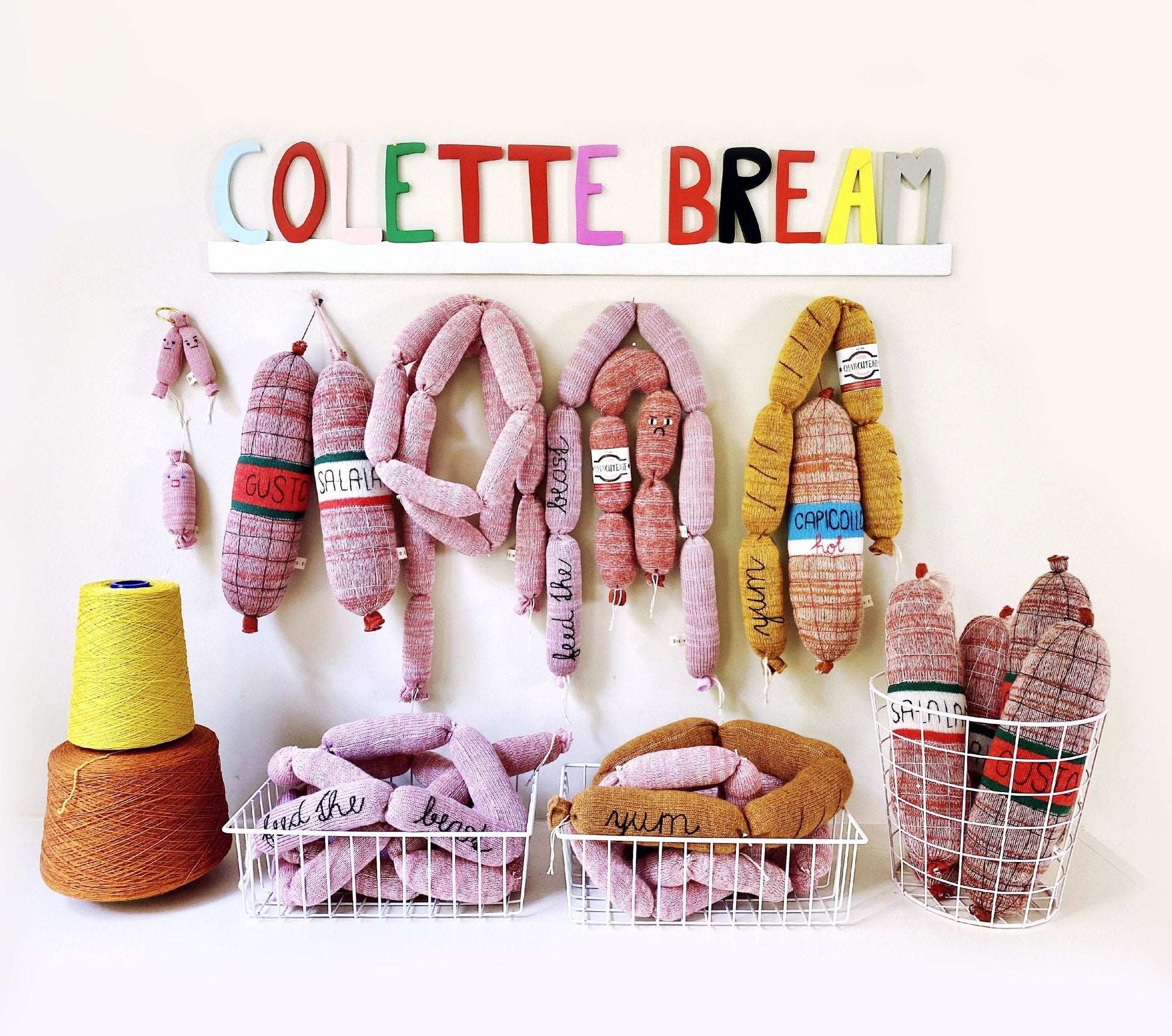 Colorful knitted plush toys resembling sausages with 'COLETTE BREAM' branding on a white background.
