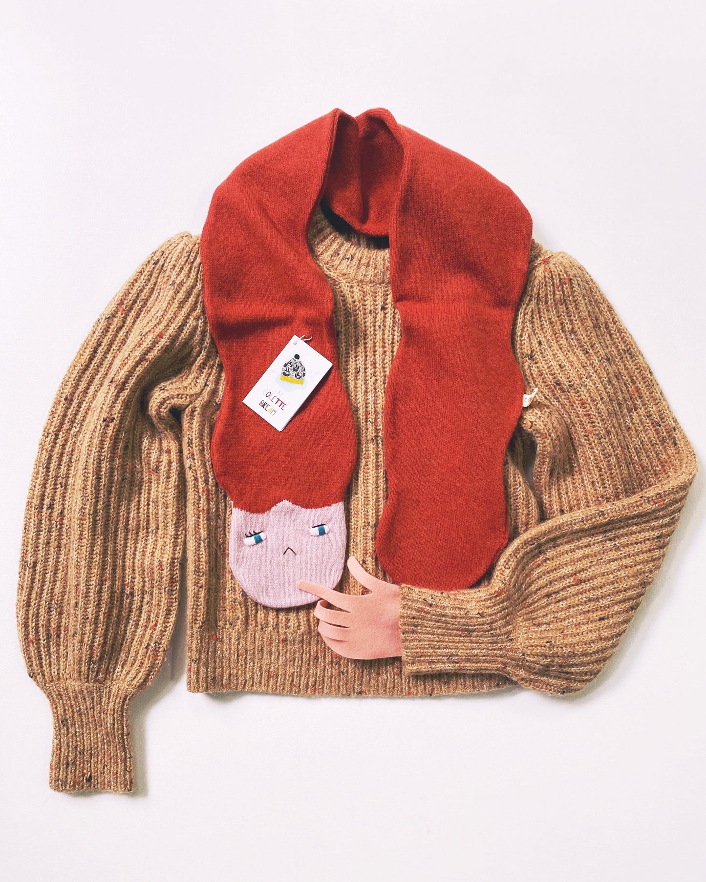Brown knitted sweater with a red scarf and cartoon character tag on a white background
