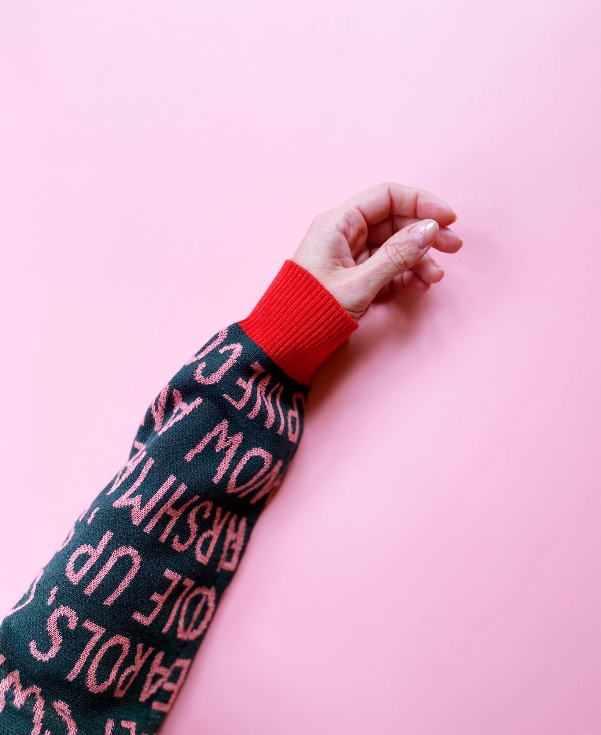 Person wearing a dark green sweater with red text on a pink background
