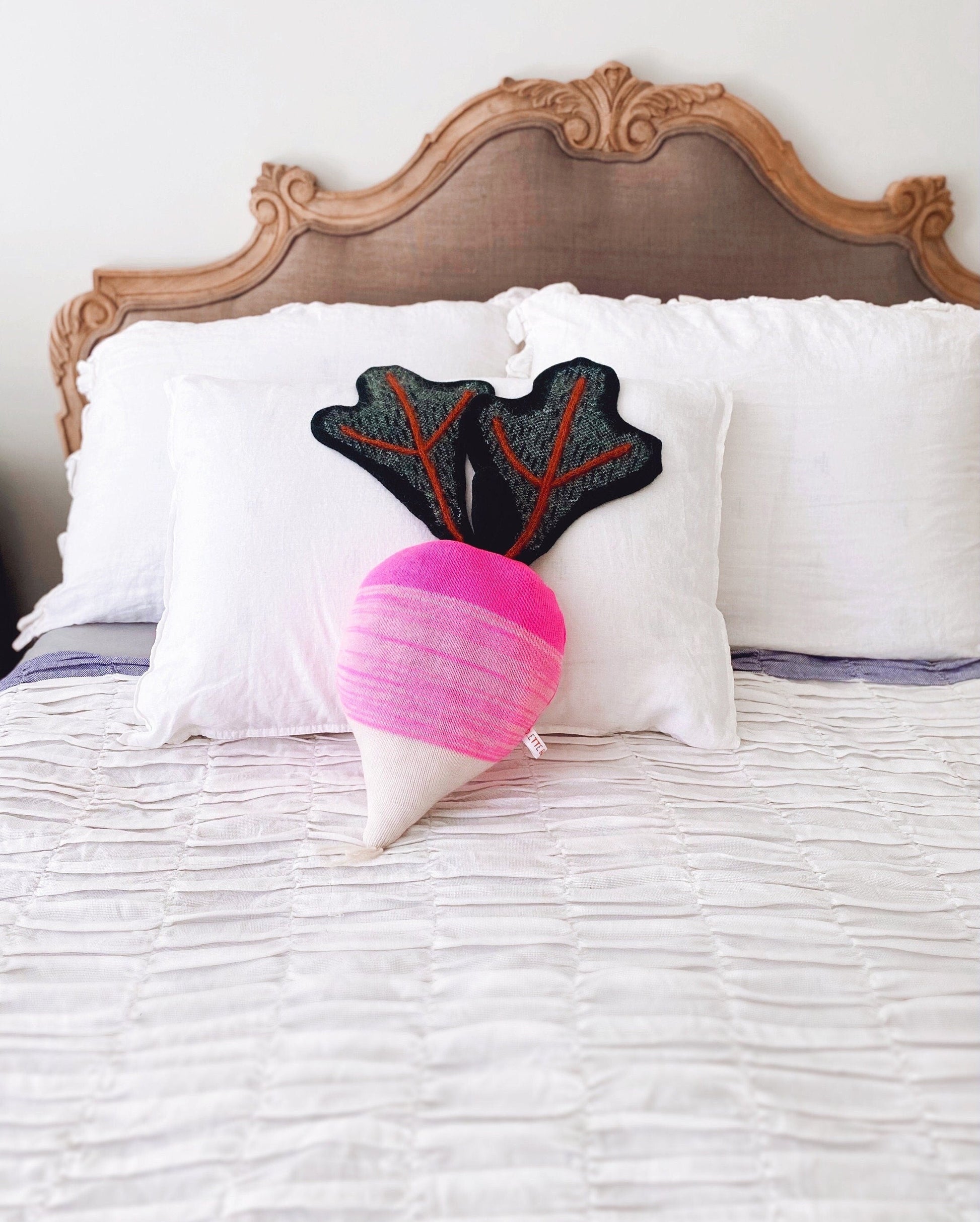Decorative radish shaped pillow with a unique design on a bed with a wooden headboard.