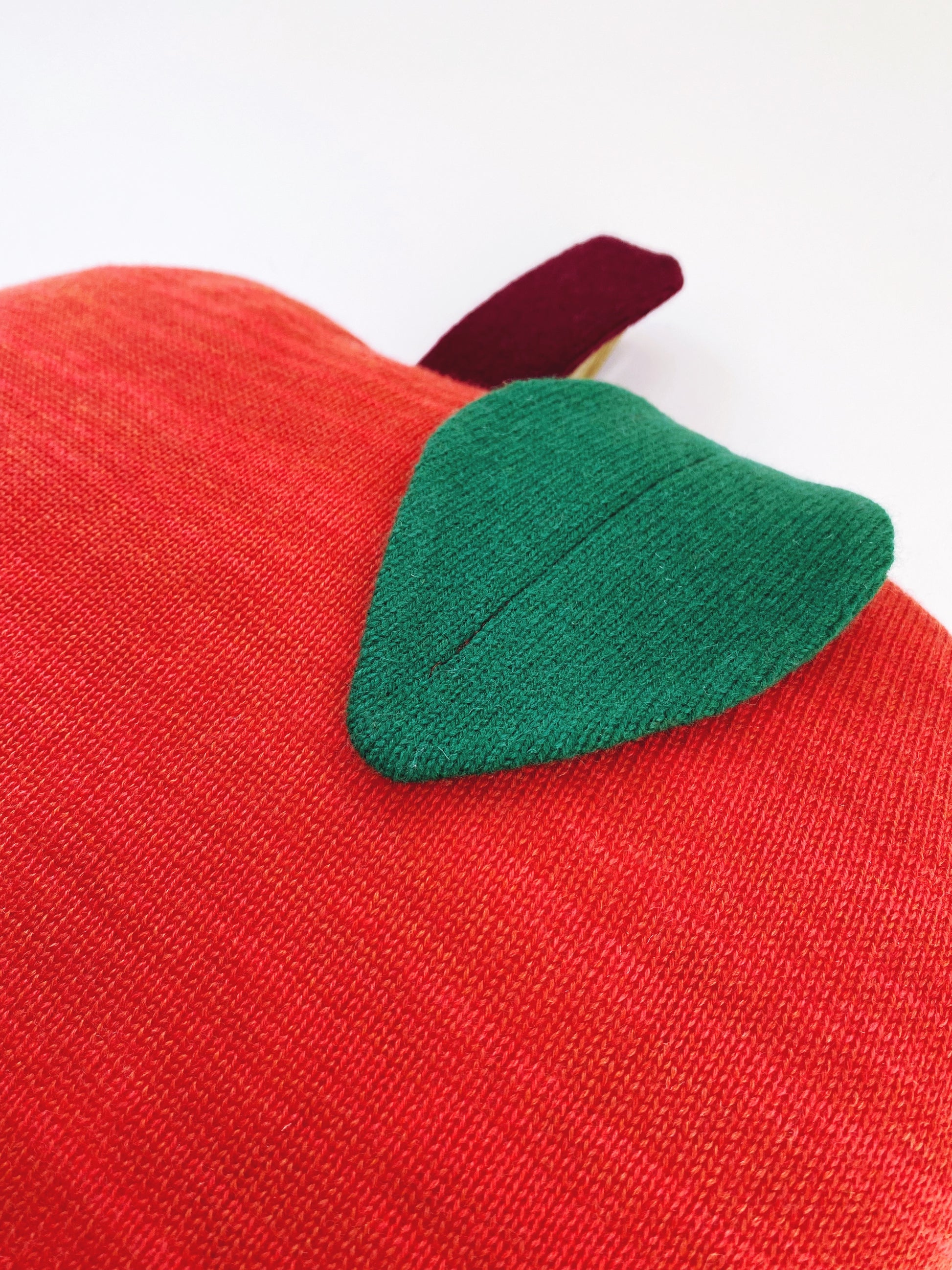 Red apple-shaped pillow with a green leaf on a white background