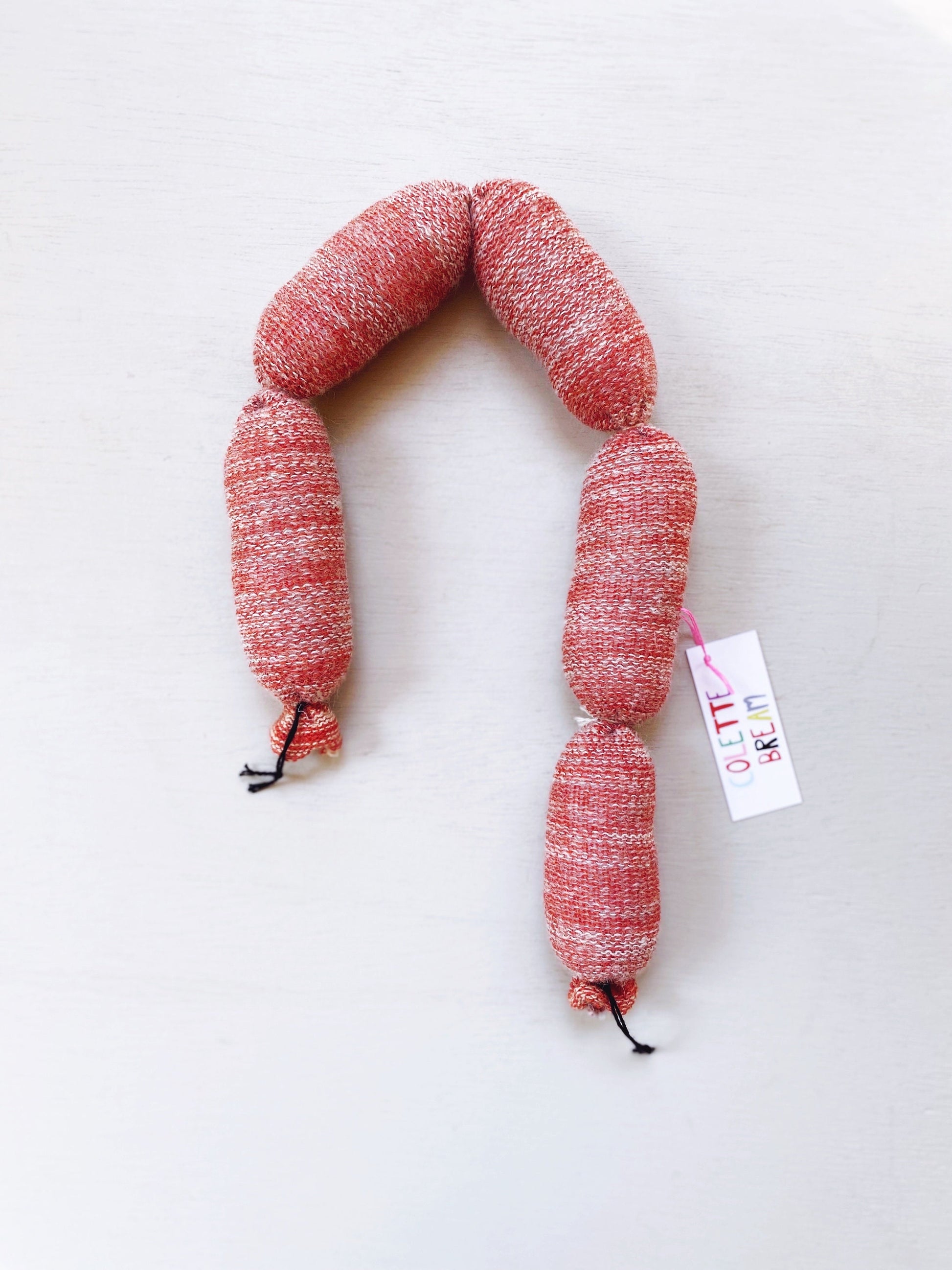 Lambswool knitted sausage on a white background with a visible brand tag.