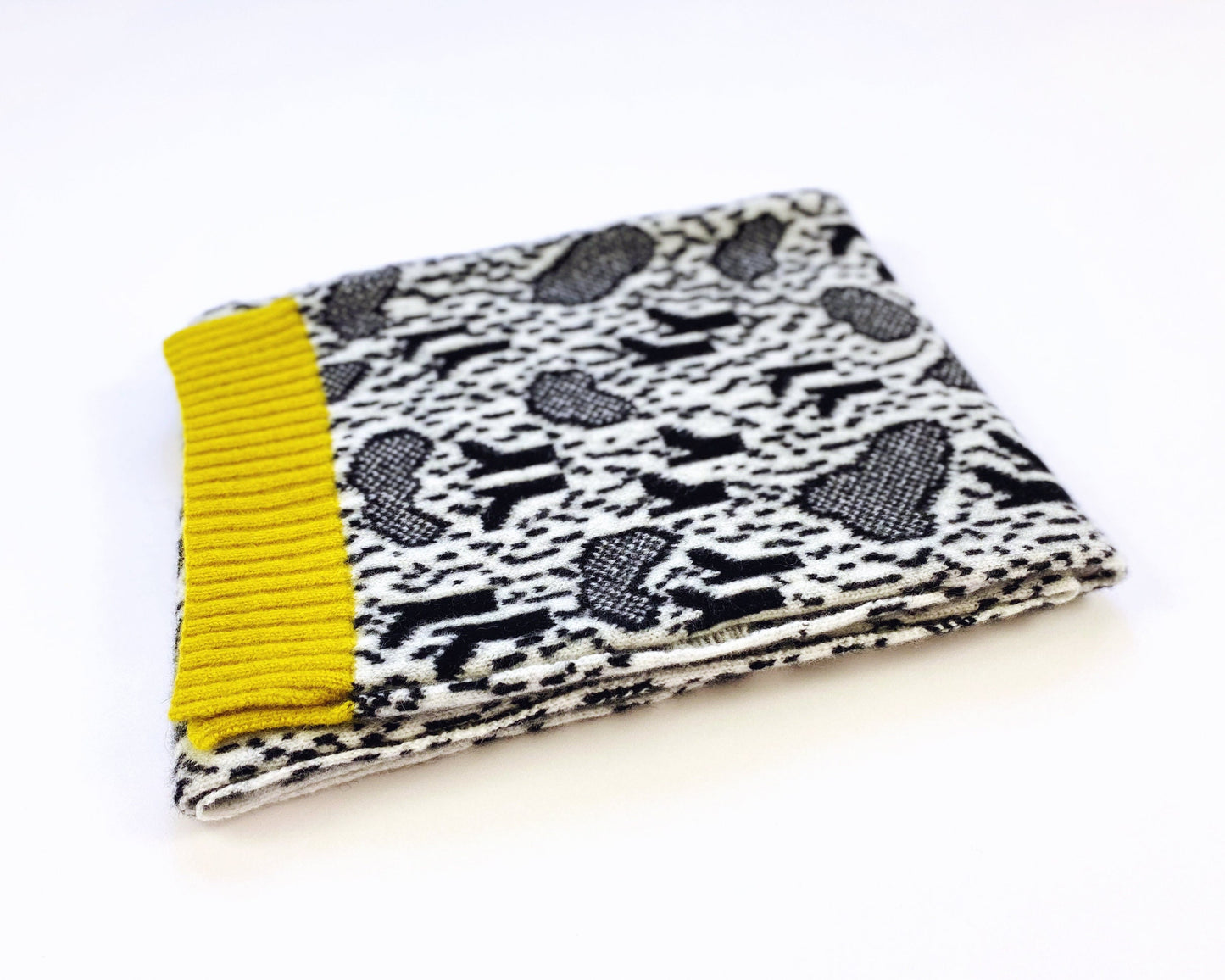 Folded knit scarf with black and white pattern and yellow trim on a white background