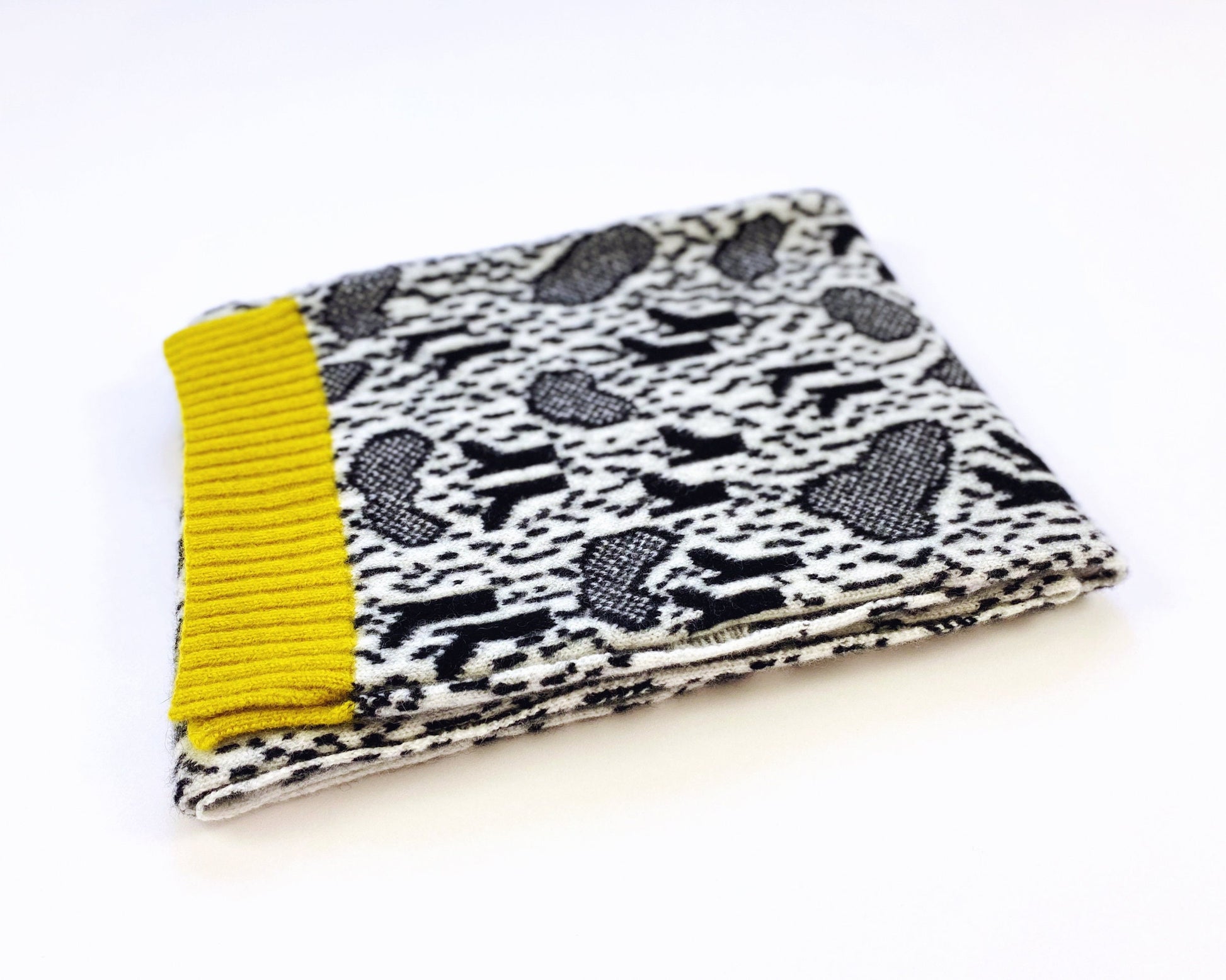 Folded knit scarf with black and white pattern and yellow trim on a white background