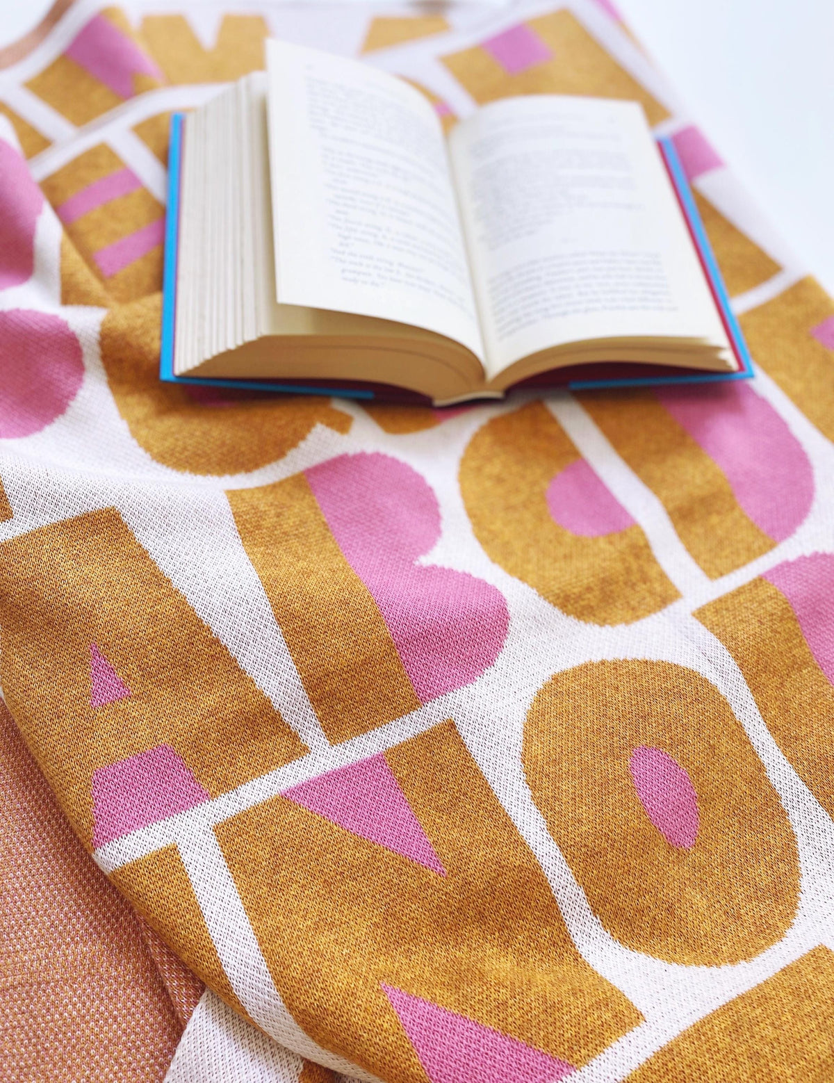 Open book on a colorful knitted blanket with geometric alphabet letters pattern
