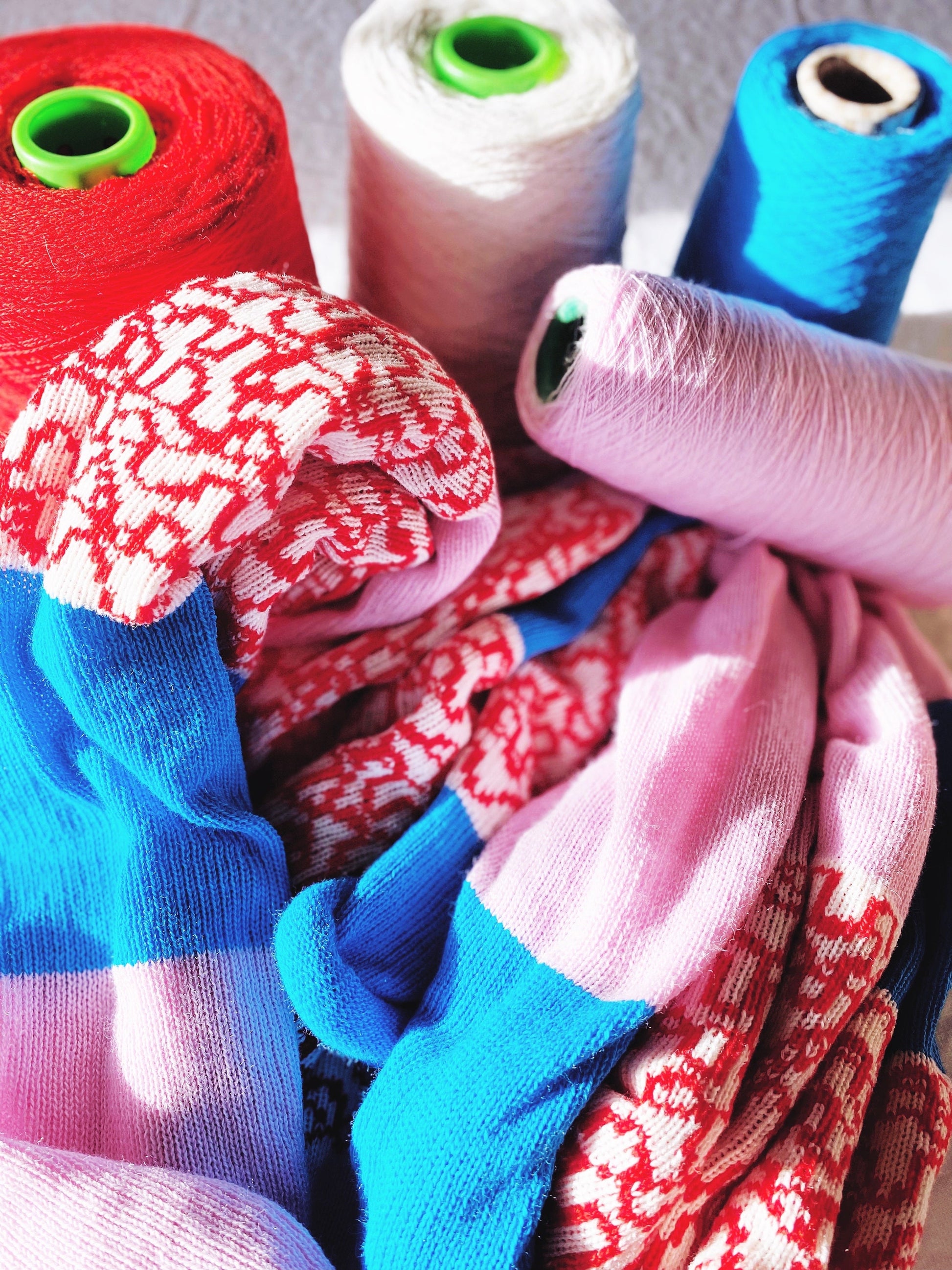 Colorful spools of yarn and knitted fabric with a close-up of a pink fabric swatch.