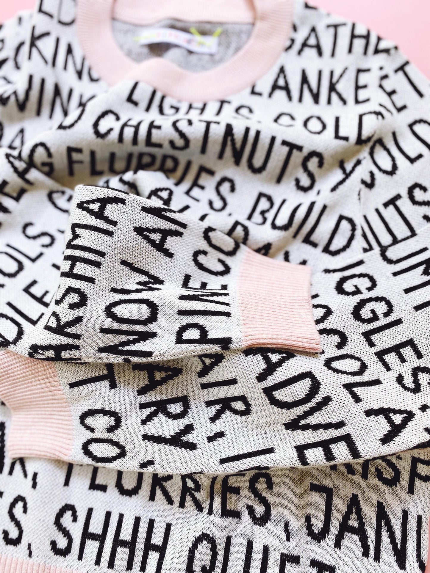 Knitted sweater with black and white festive christmas text pattern on a pink background