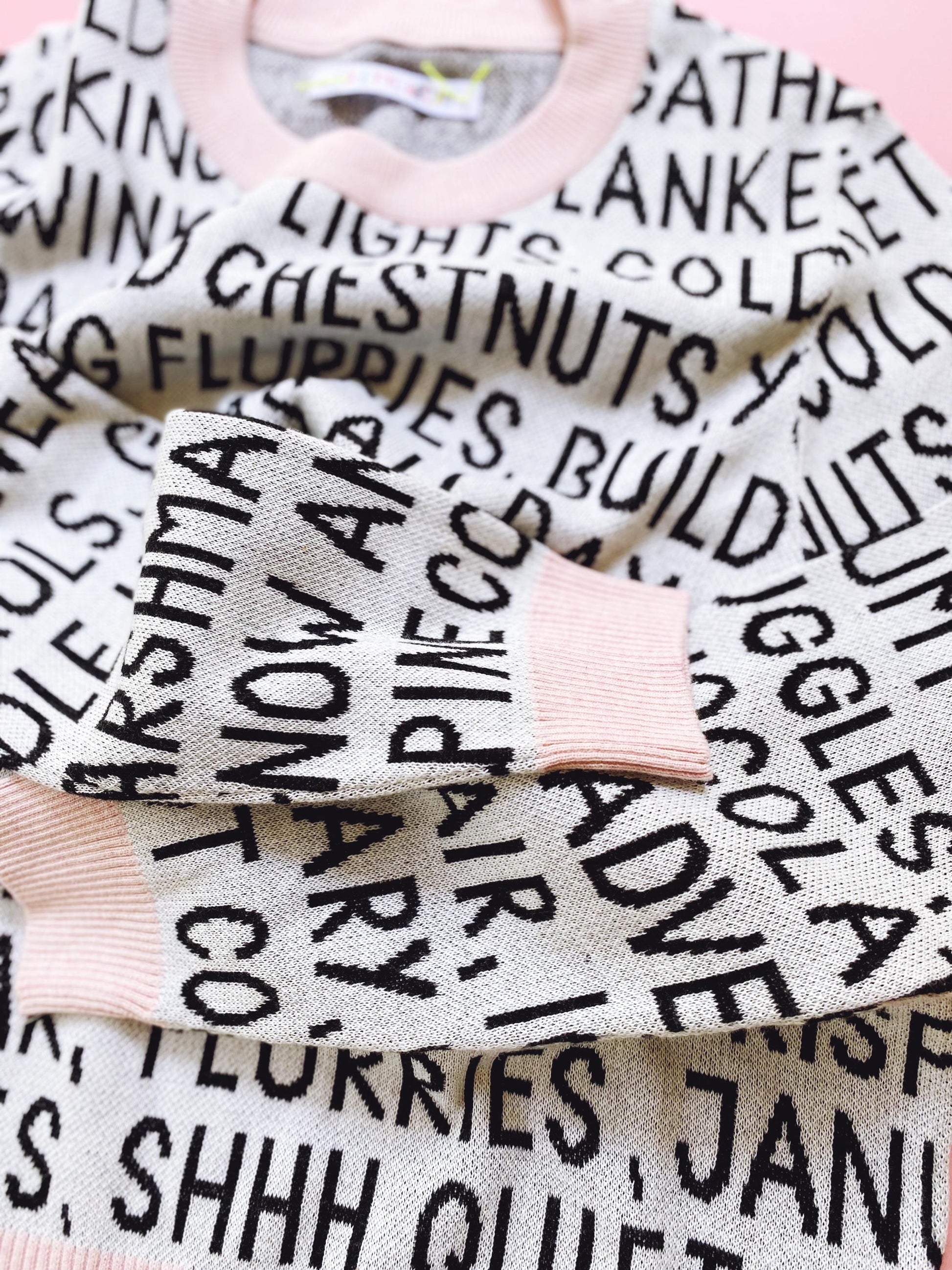 Knitted sweater with black and white festive christmas text pattern on a pink background