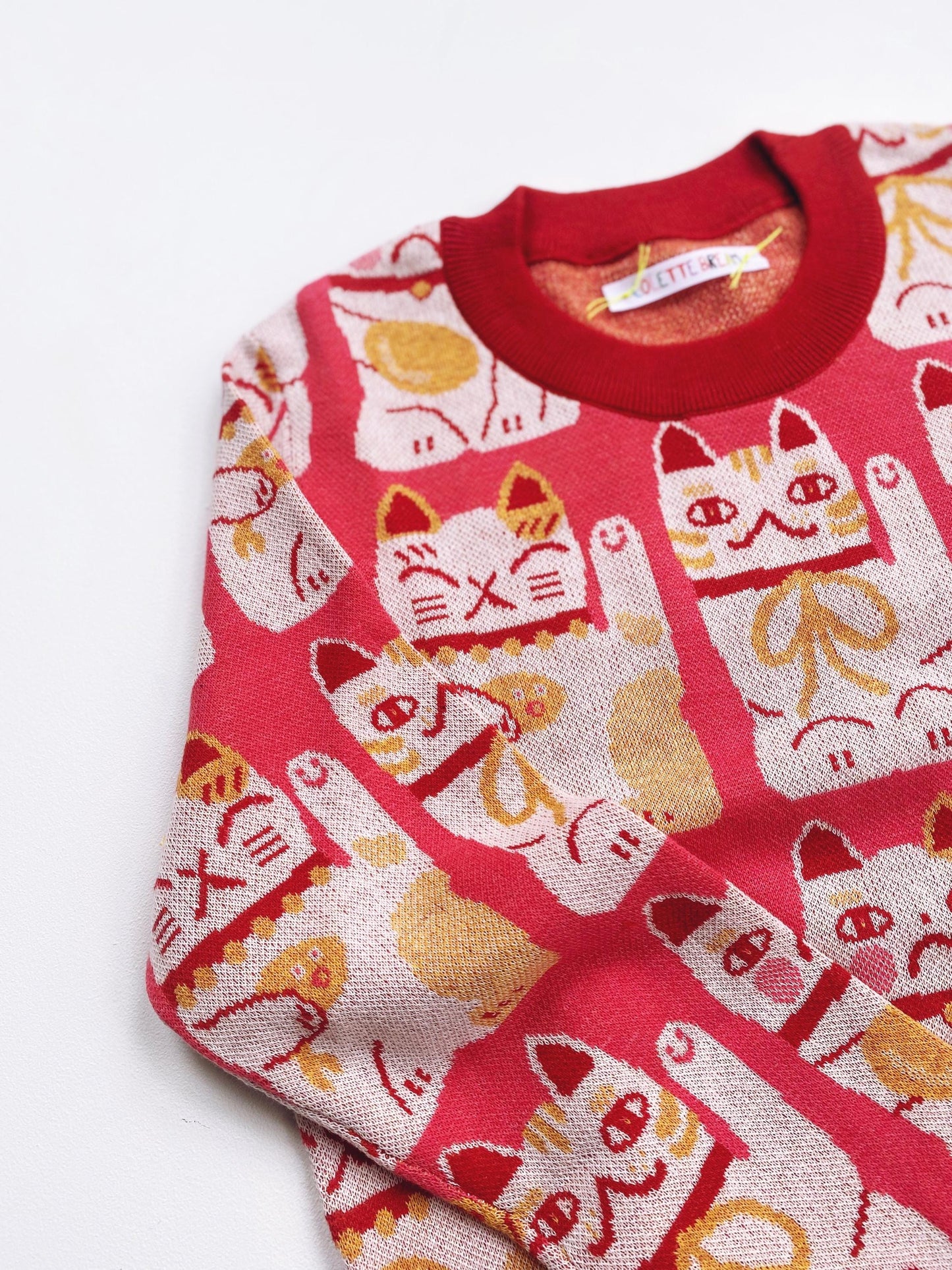 Pink knitted sweater with maneki neko cat pattern on a white background