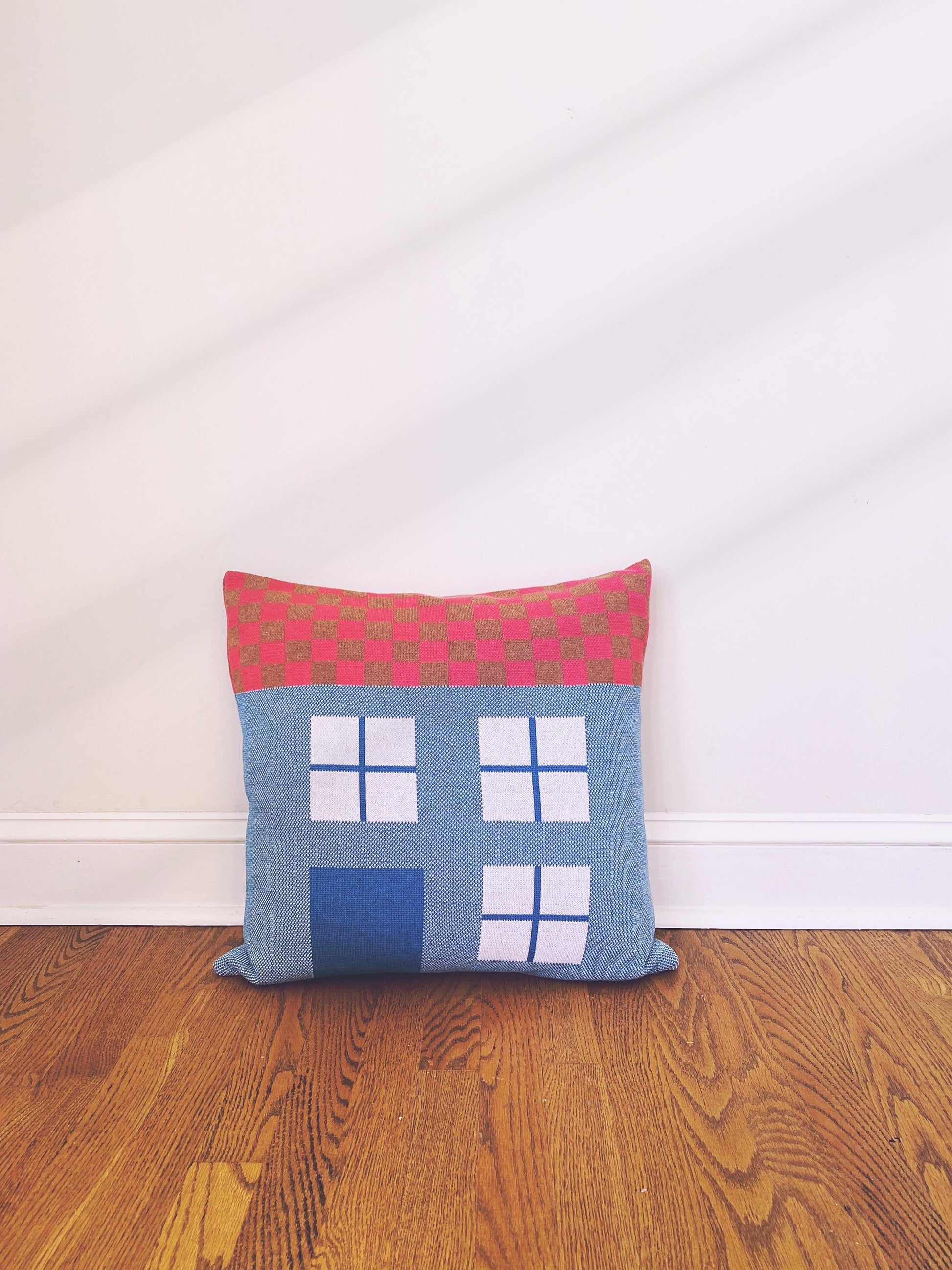 Decorative house shaped pillow with a checkered pattern on a wooden floor against a white wall