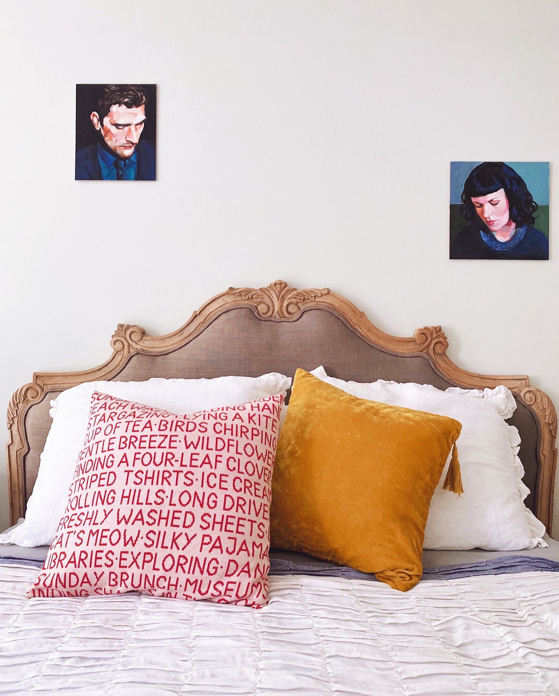 Bed with decorative pillows and headboard against a white wall with two small framed pictures.