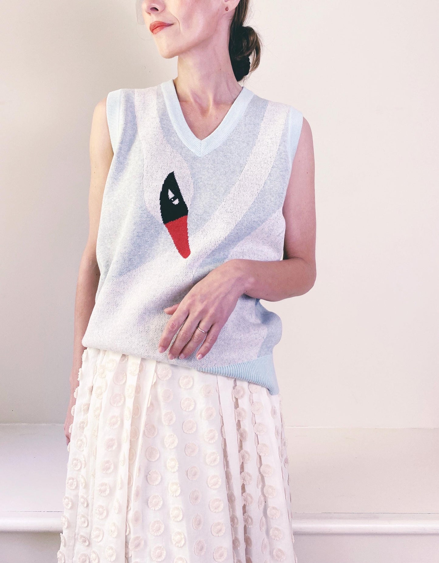 Woman wearing a sleeveless sweater vest with a white swan design on a plain background