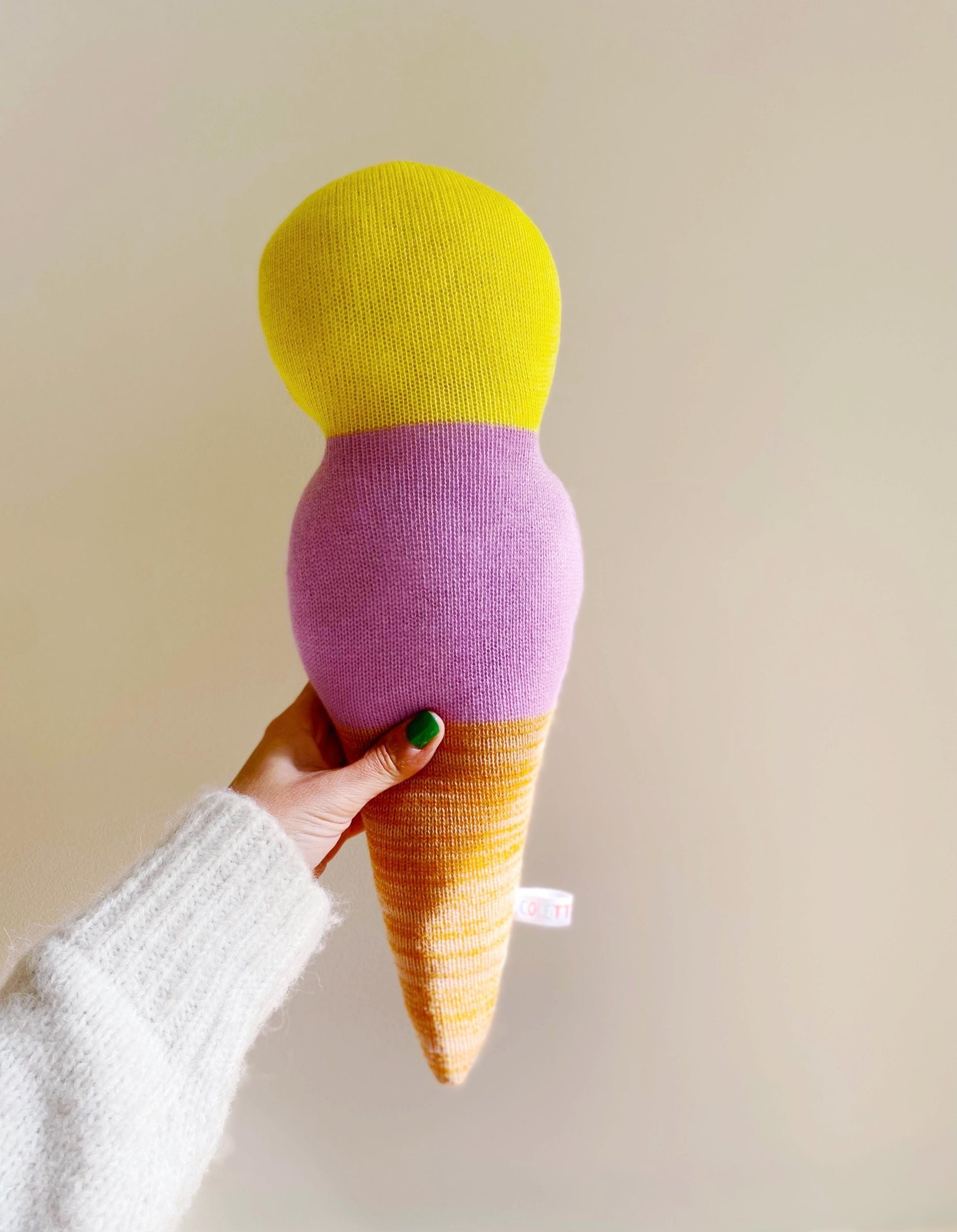 Hand holding a colorful ice cream cone-shaped pillow against a plain background