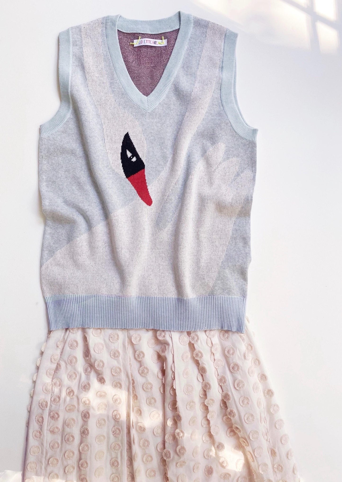Light blue sleeveless sweater vest with a white swan design on a white background