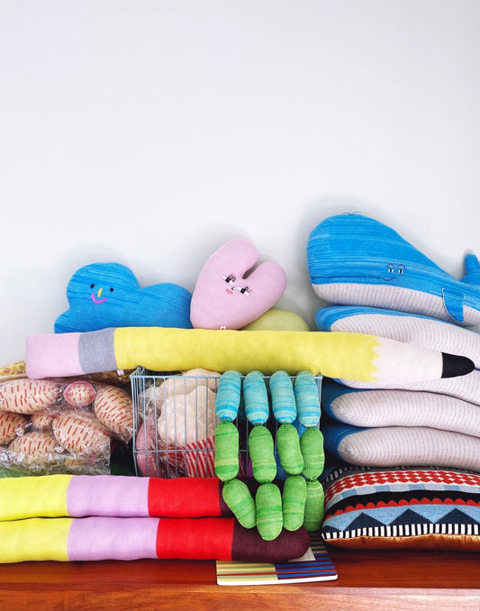 Stack of colorful knitted plush toys and pillows on a wooden surface with a white background