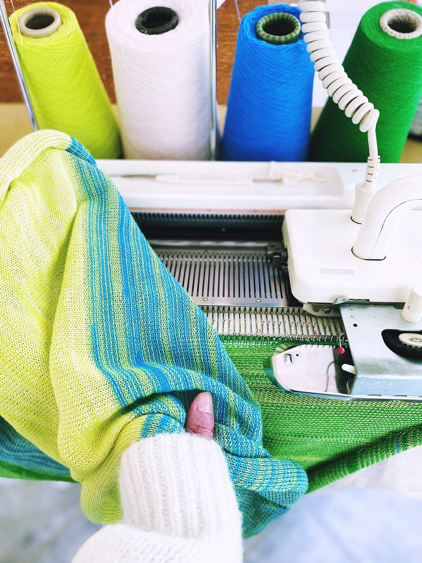 Close-up of a knitting machine with colorful fabric and spools of yarn thread.