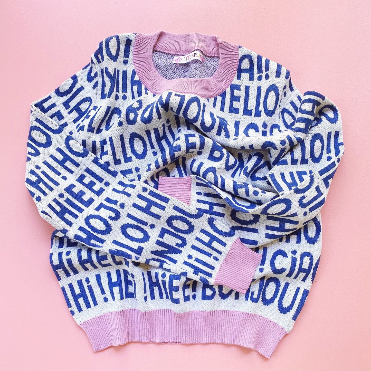 Knit white and blue sweater with 'HELLO!' greetings text on a pink background