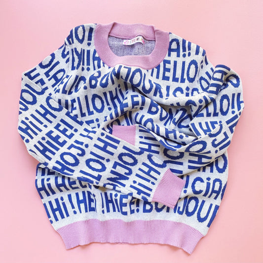 Knit white and blue sweater with 'HELLO!' greetings text on a pink background
