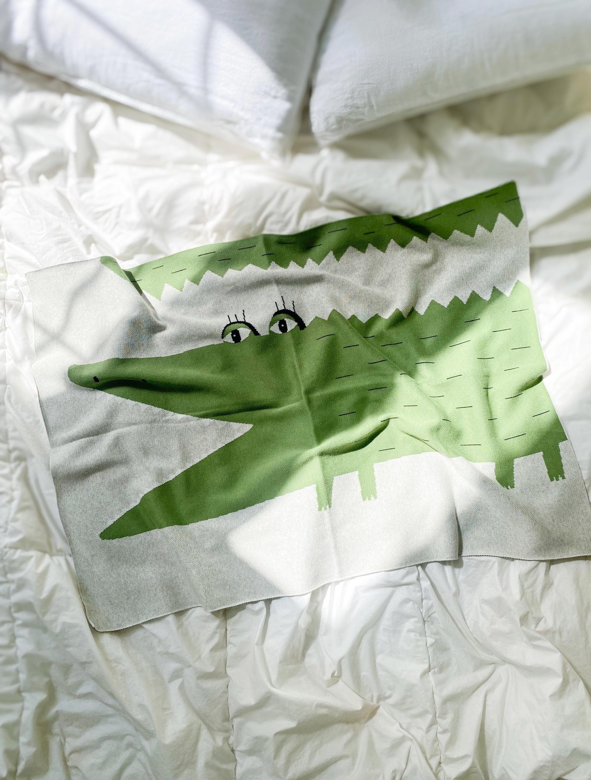 Knit baby blanket with green cartoon crocodile design on white bed sheets