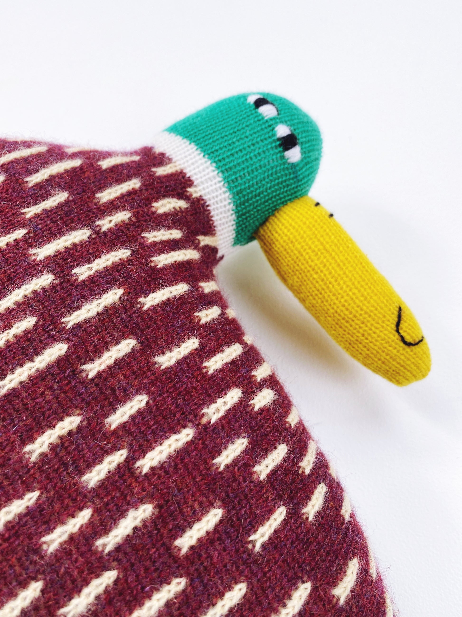 Knitted lambswool toy duck with a green head, yellow body, and red body with white patterns on a white background