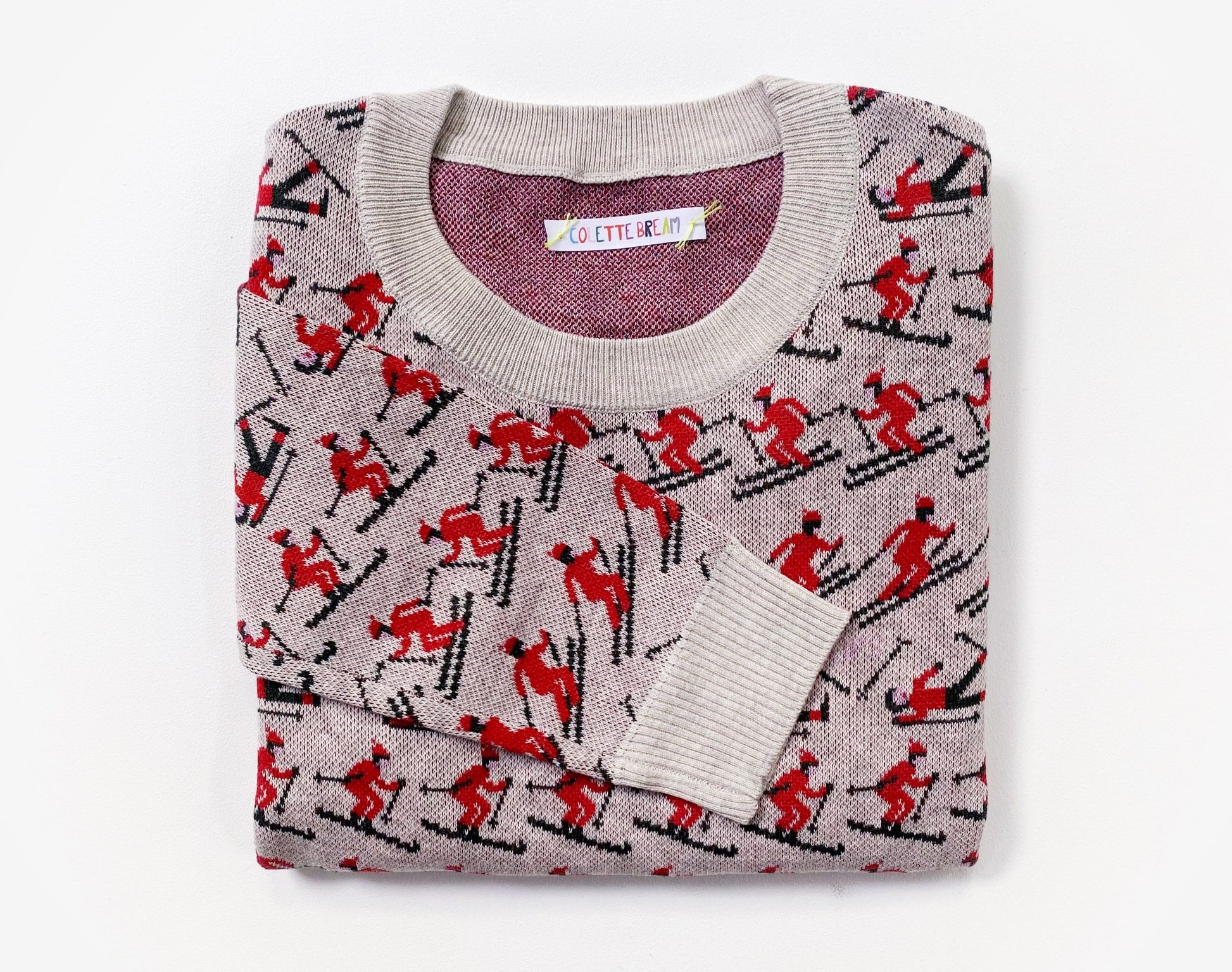 Folded sweater with red and black pattern of skiers skiing on a white background