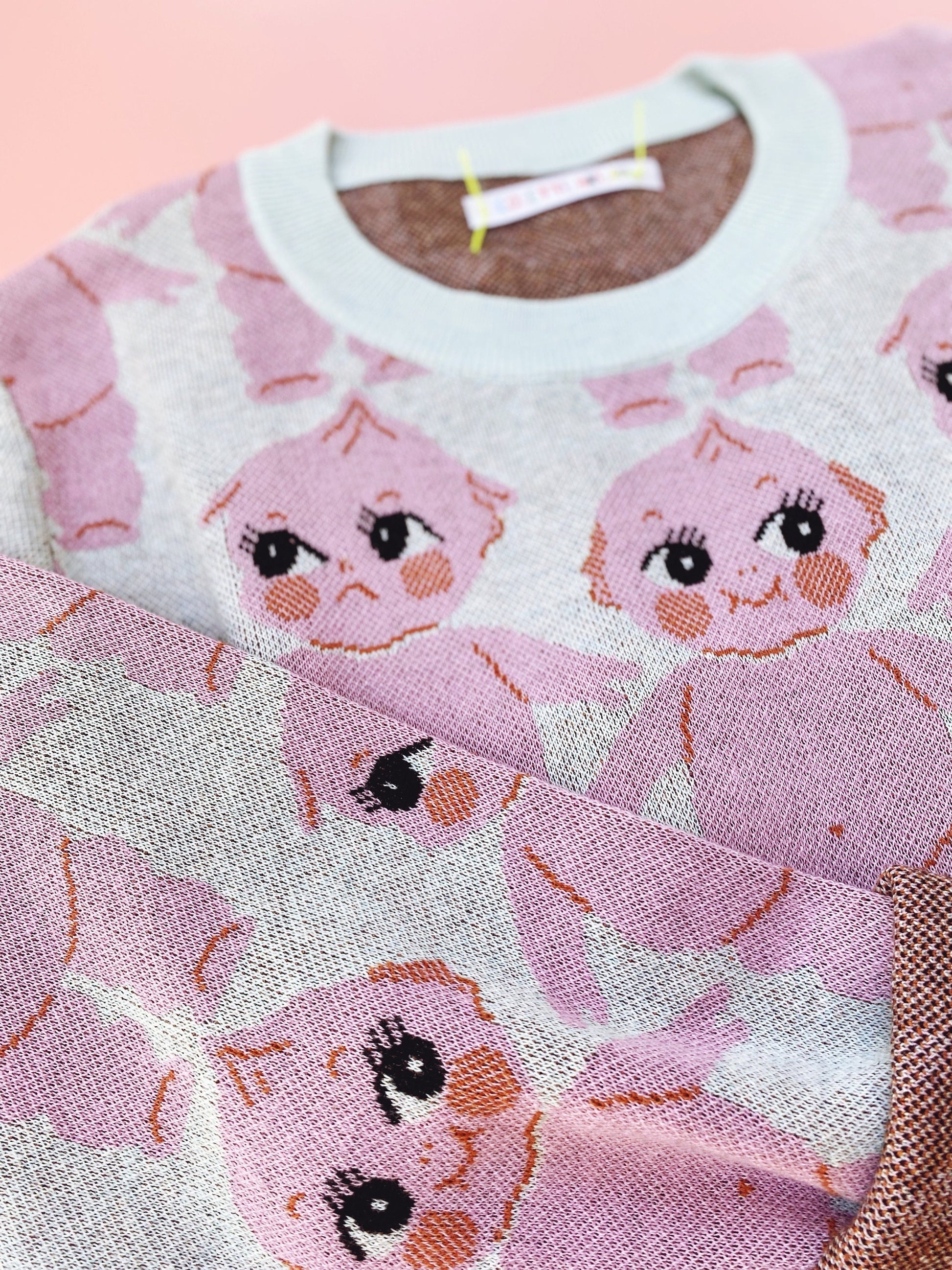 Pink sweater with cartoon kewpie doll character design on a pink background