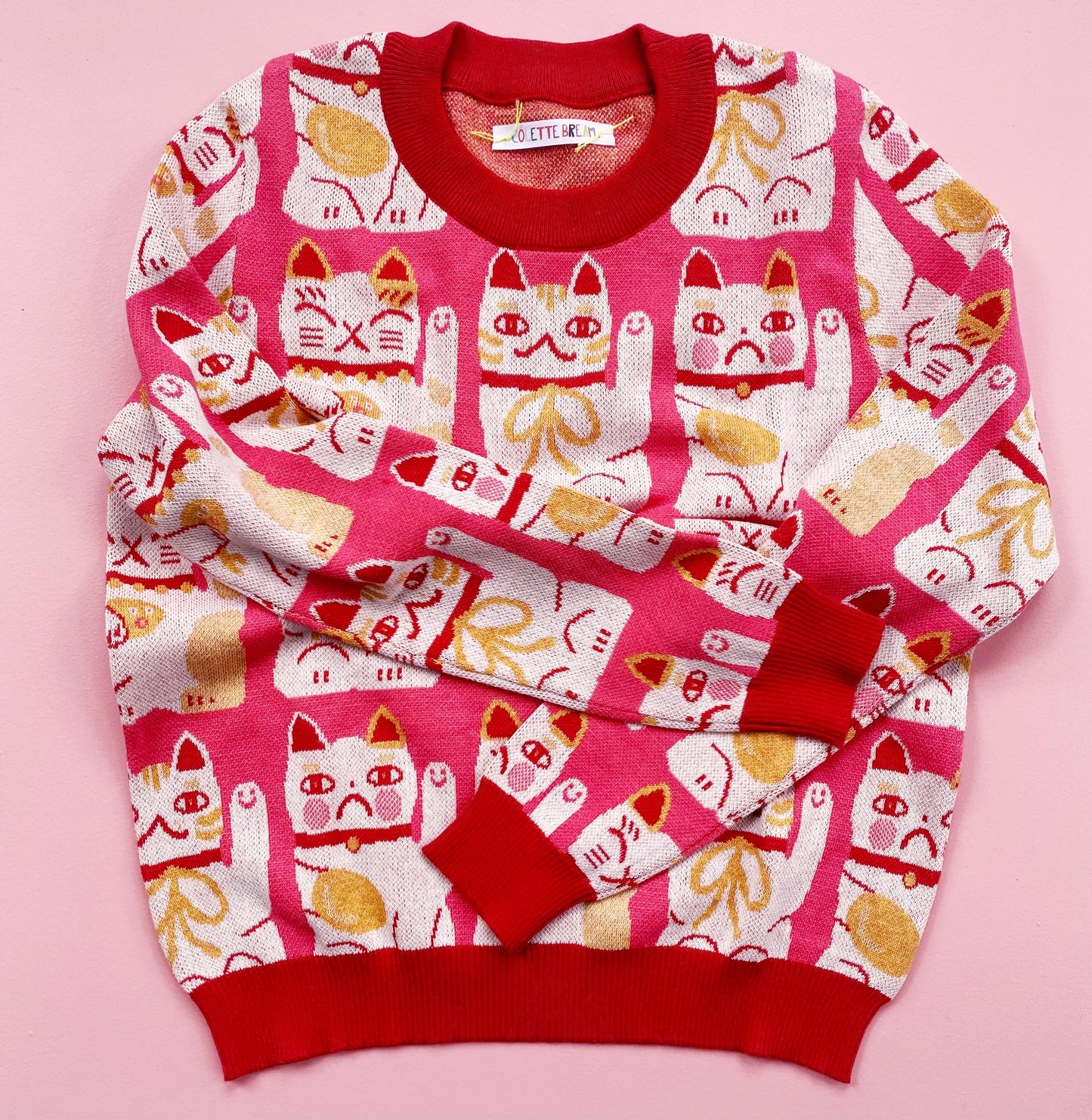 Pink sweater with maneki neko cat pattern on a pink background