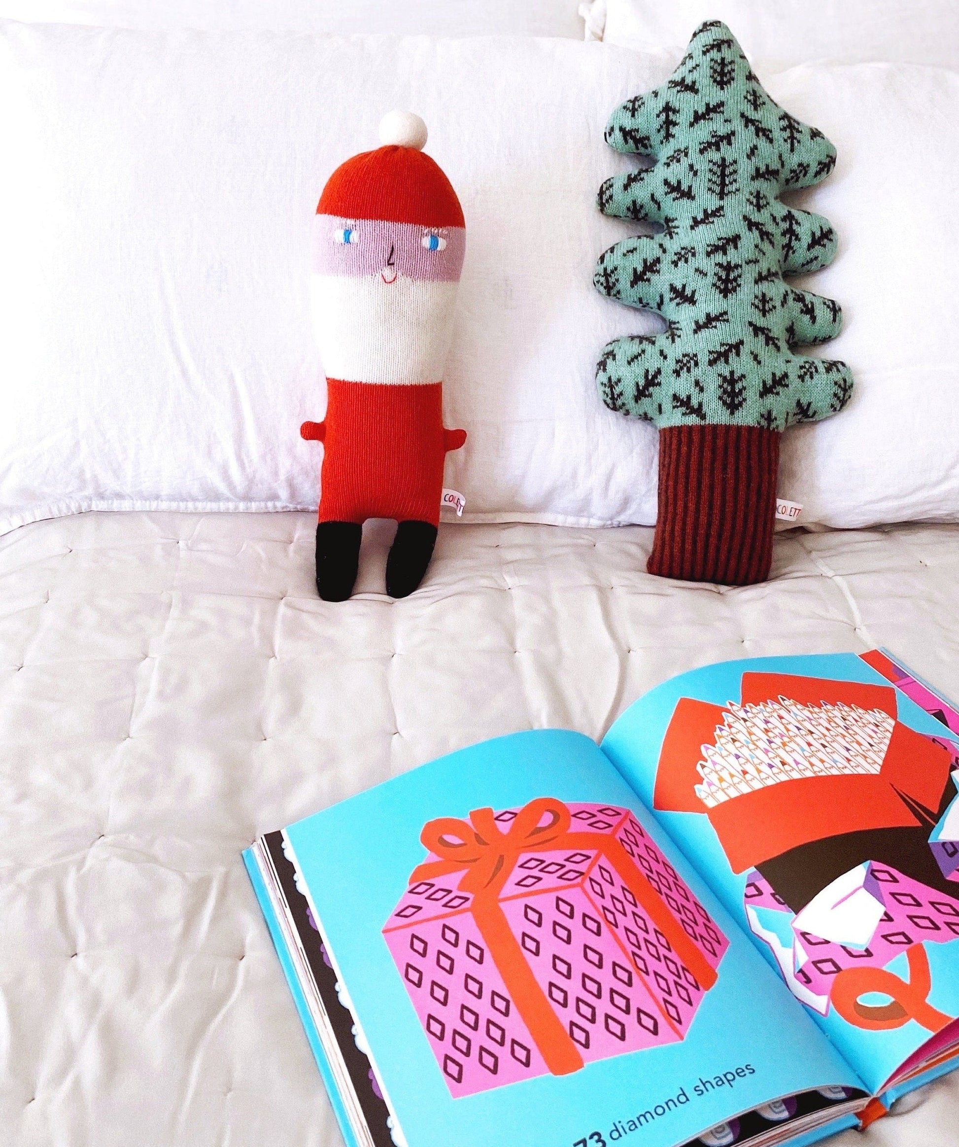 Santa plush and tree-shaped pillow next to an open book on a white surface