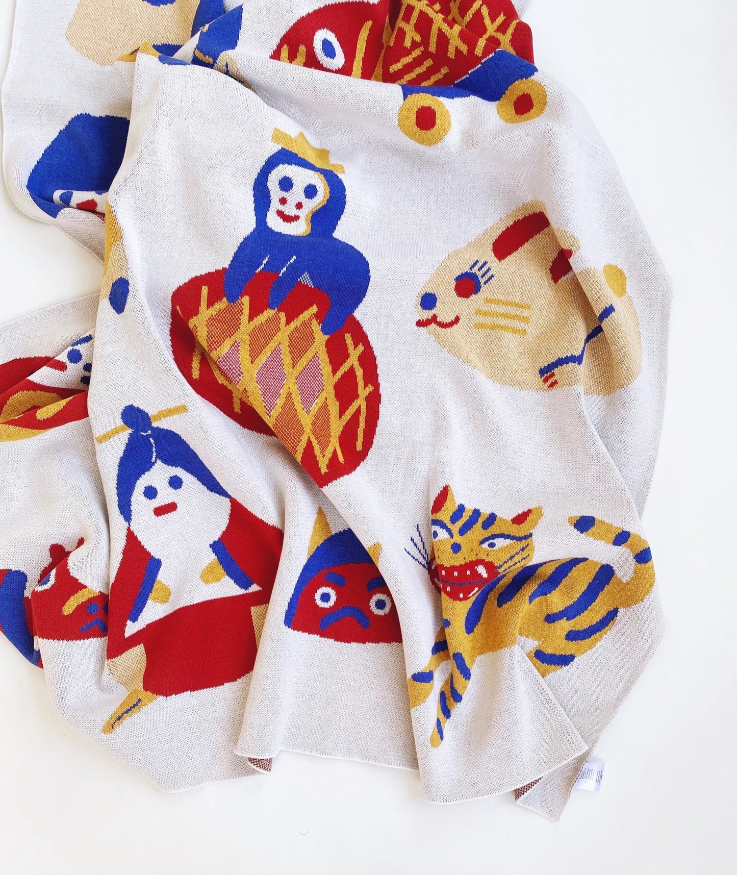 Knitted blanket throw with colorful animal illustrations and other japanese characters and folk toys on a white background