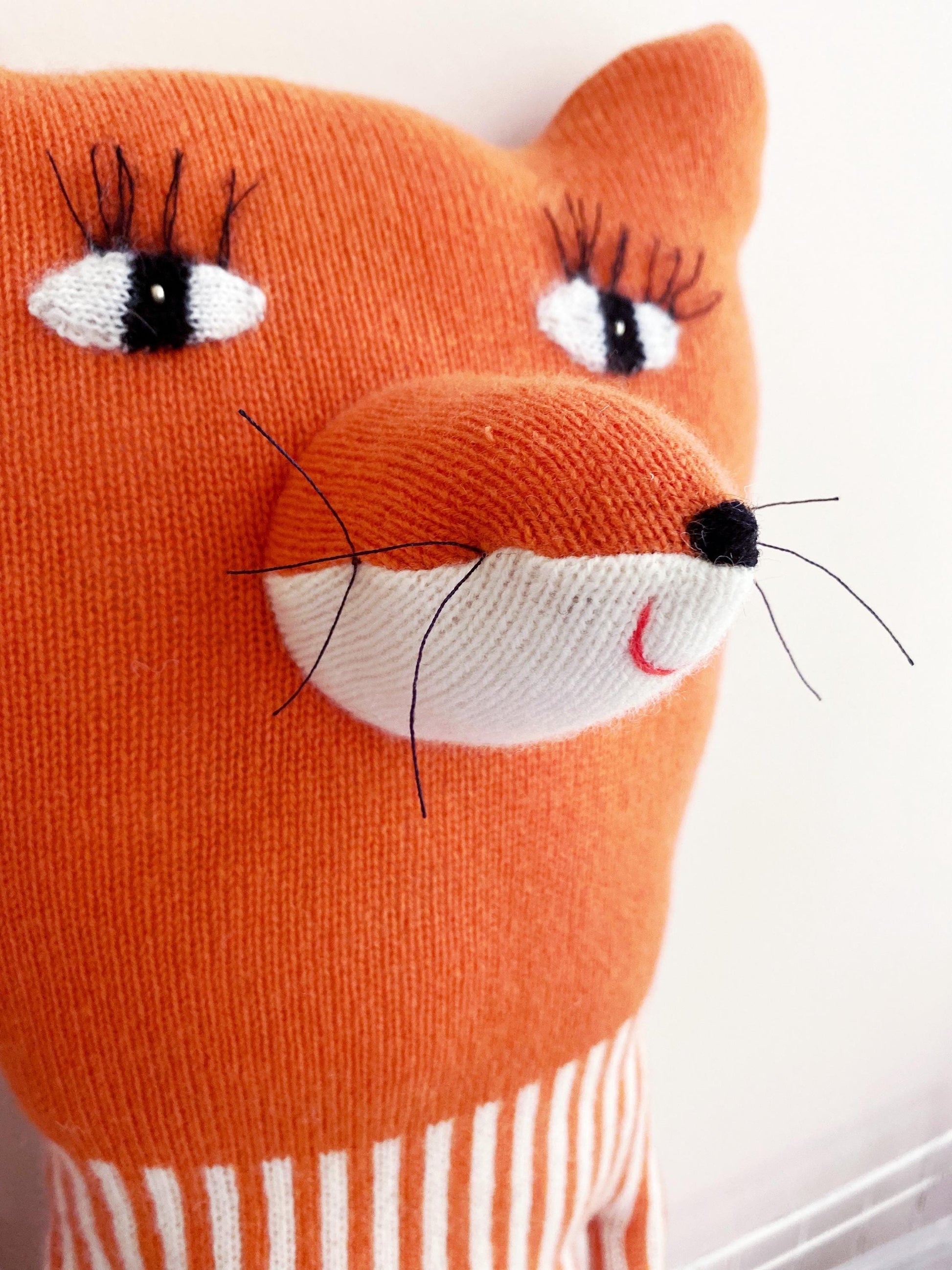 Close-up of an orange fox-shaped pillow with a white stripe on a white background