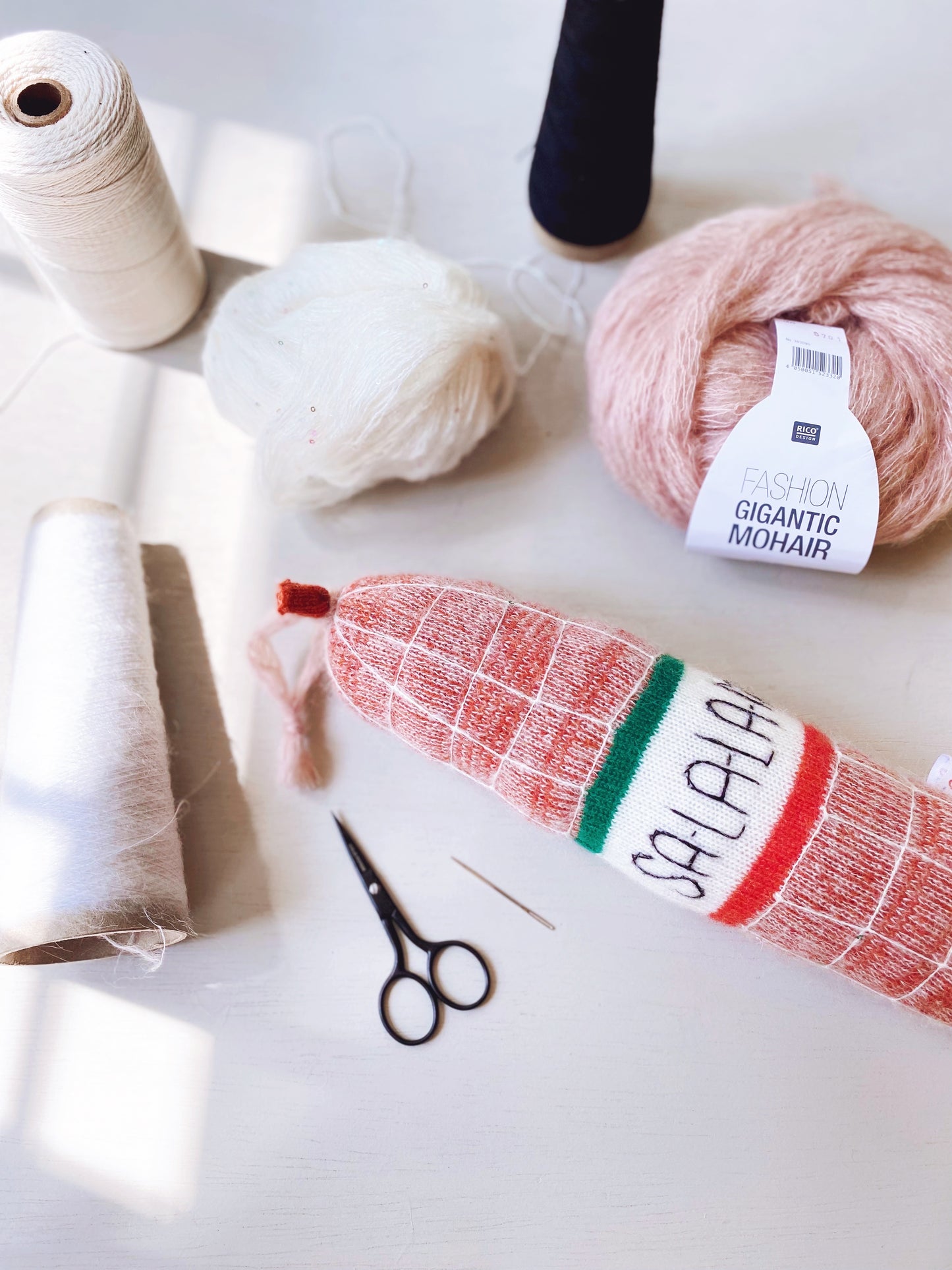 Yarn skeins, scissors, and a knitted salami with 'Salala' branding on a light surface.