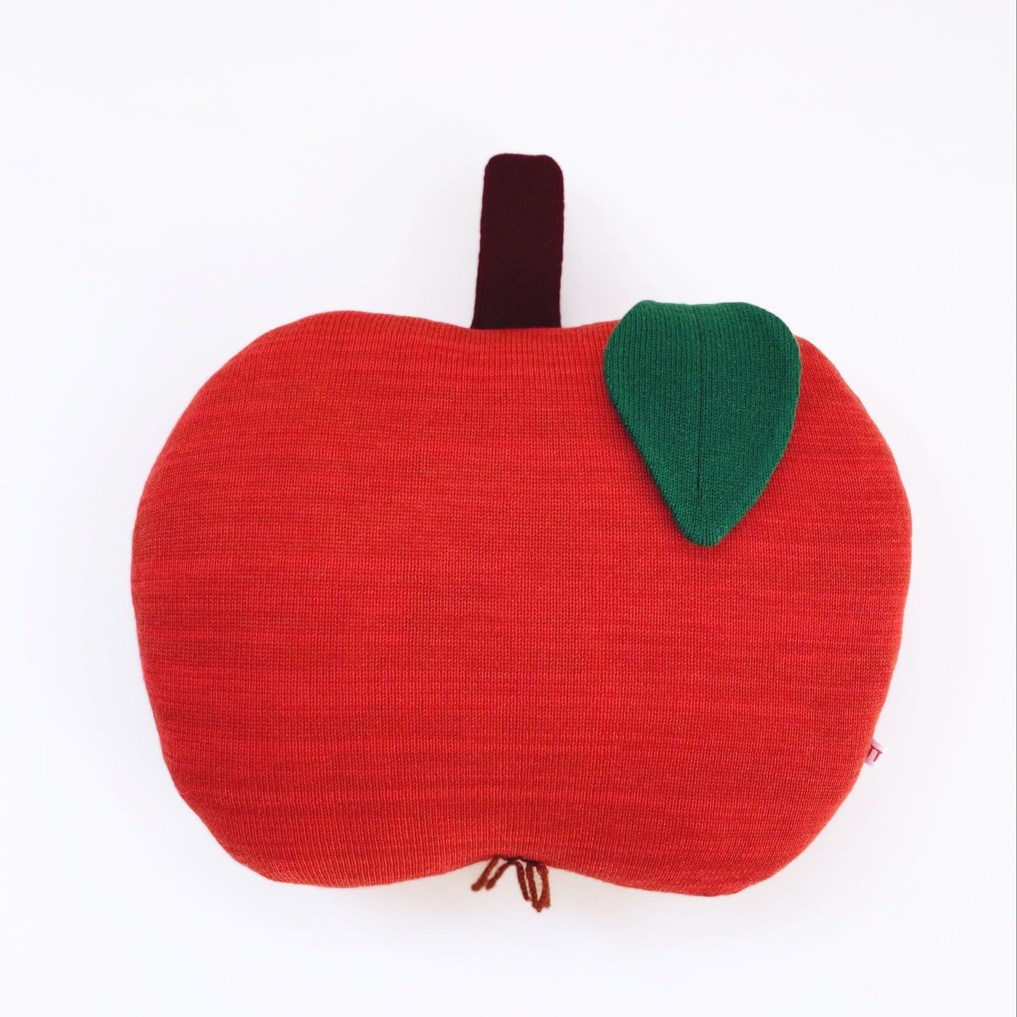 Red apple-shaped cushion with a green leaf on a white background