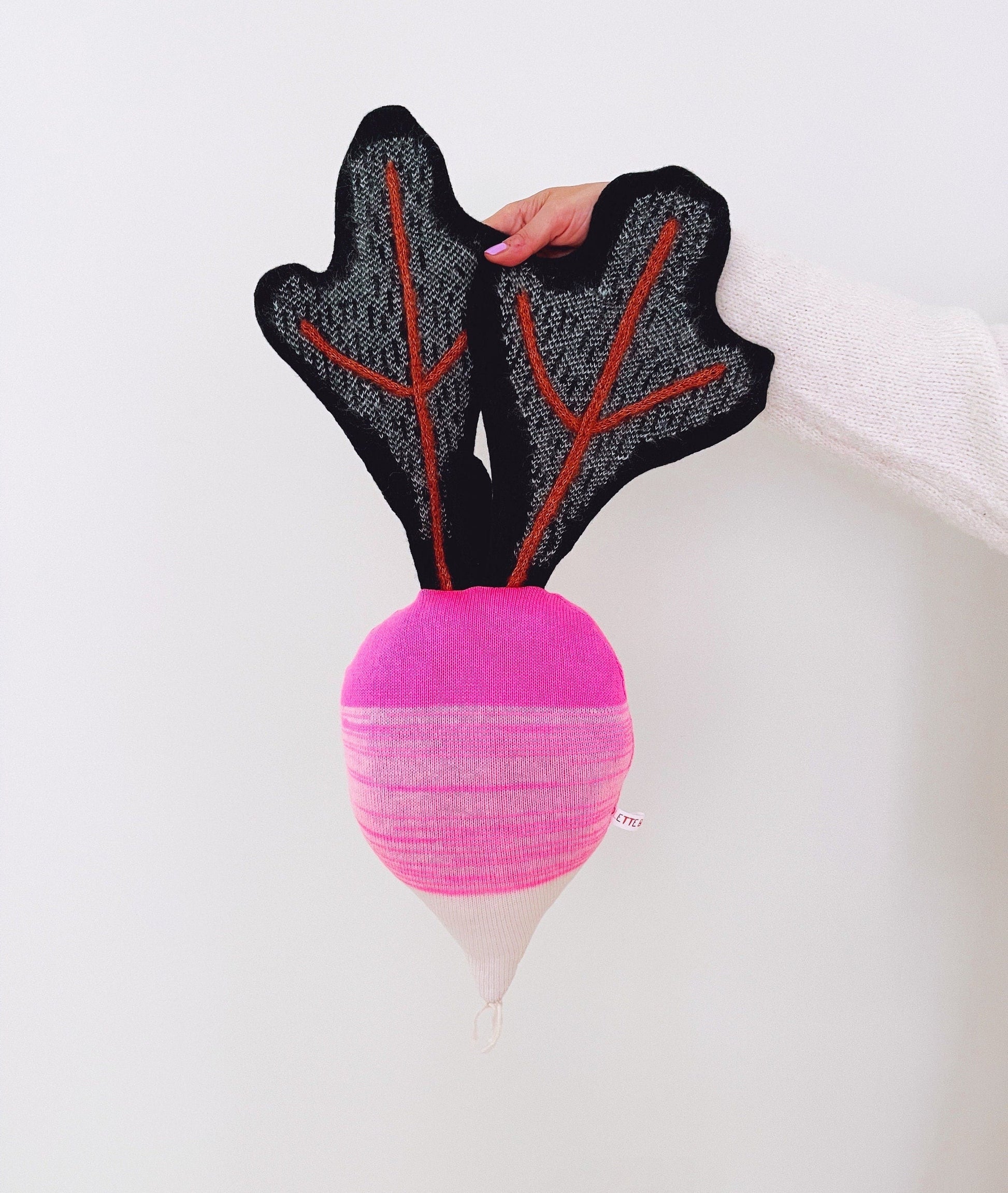 Pink knitted decorative pillow resembling a radish on a white background