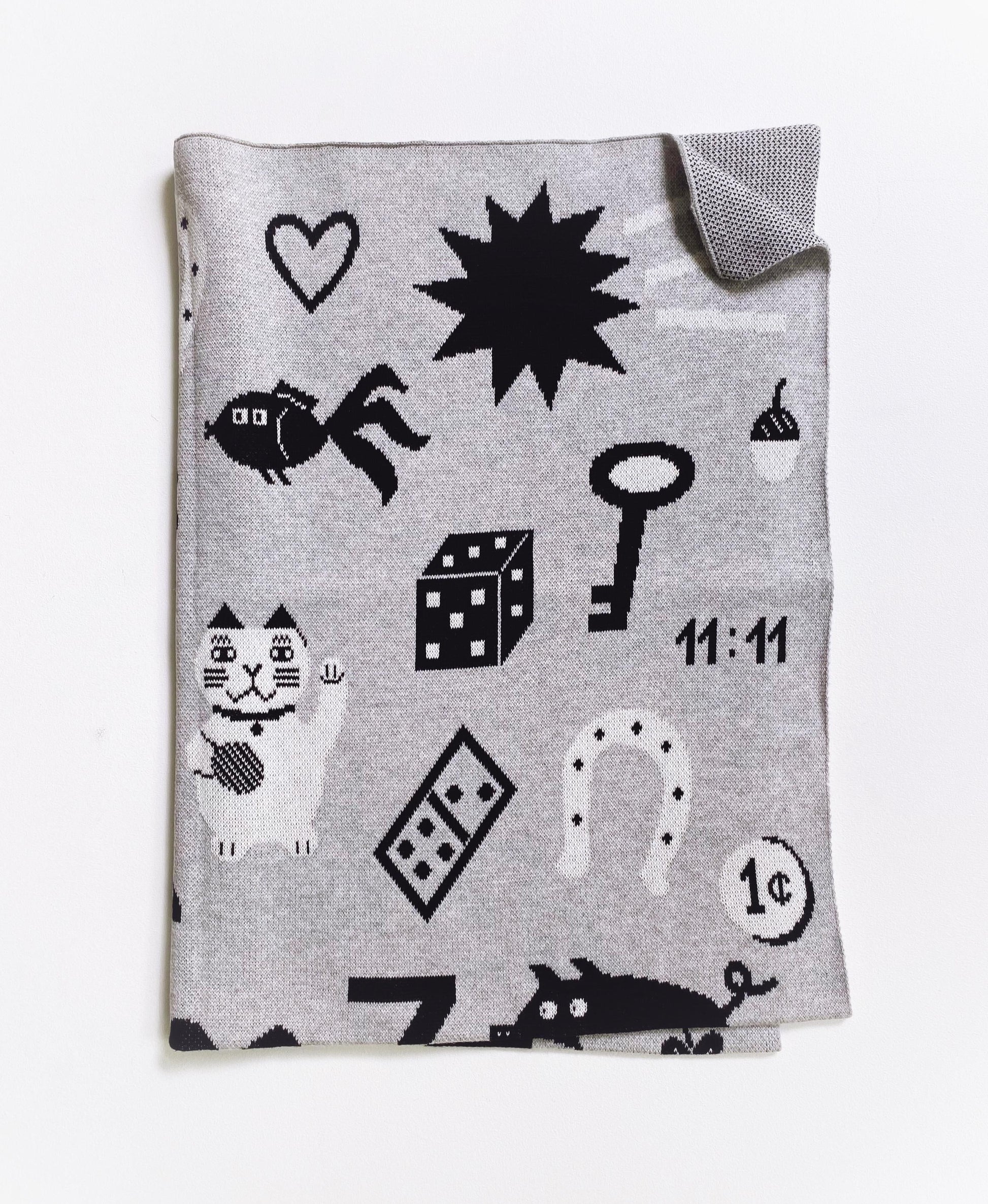 Gray knit blanket with black and white good luck charm symbols pattern on a white background