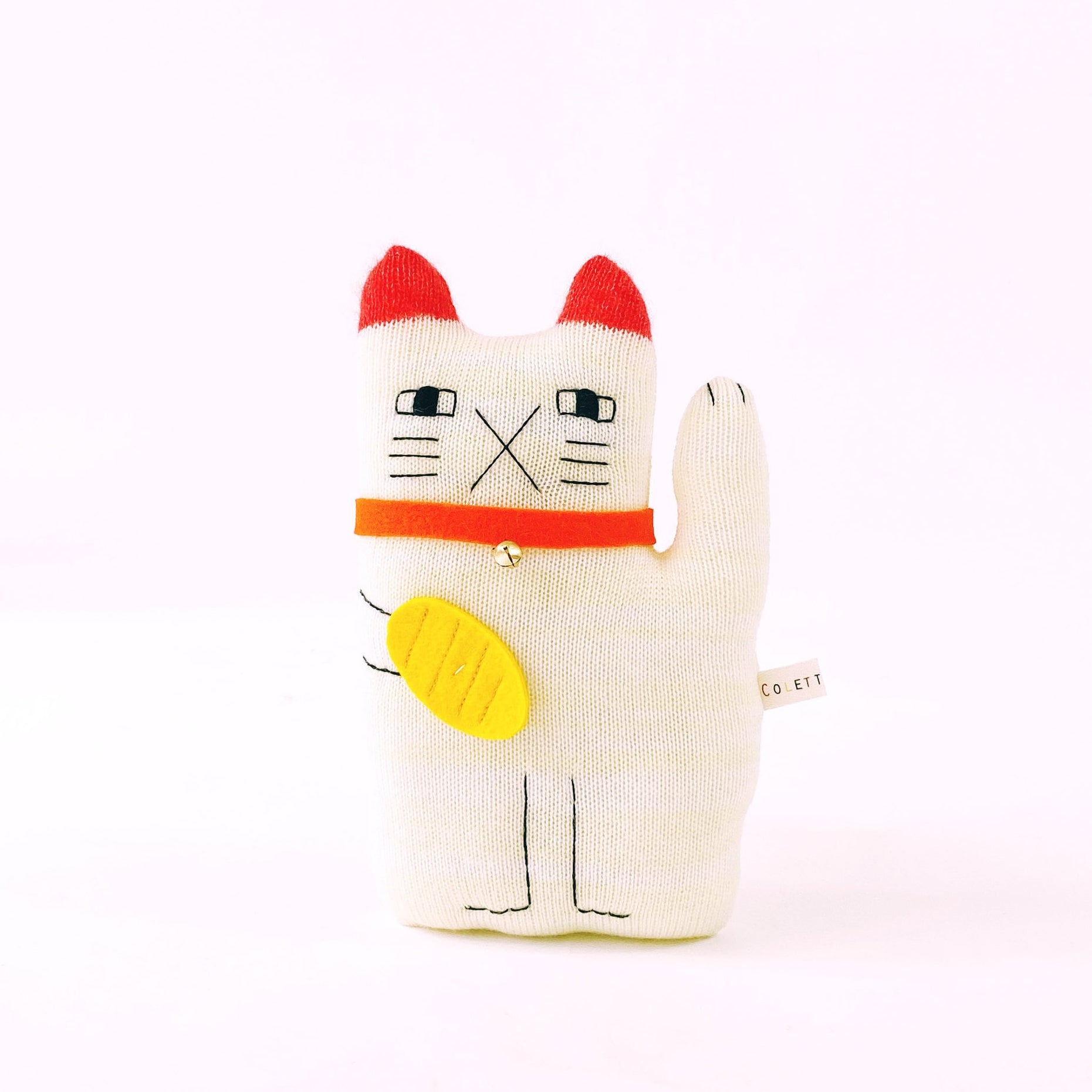 Cat-shaped maneki neko plush toy with red ears and yellow ornament on a white background