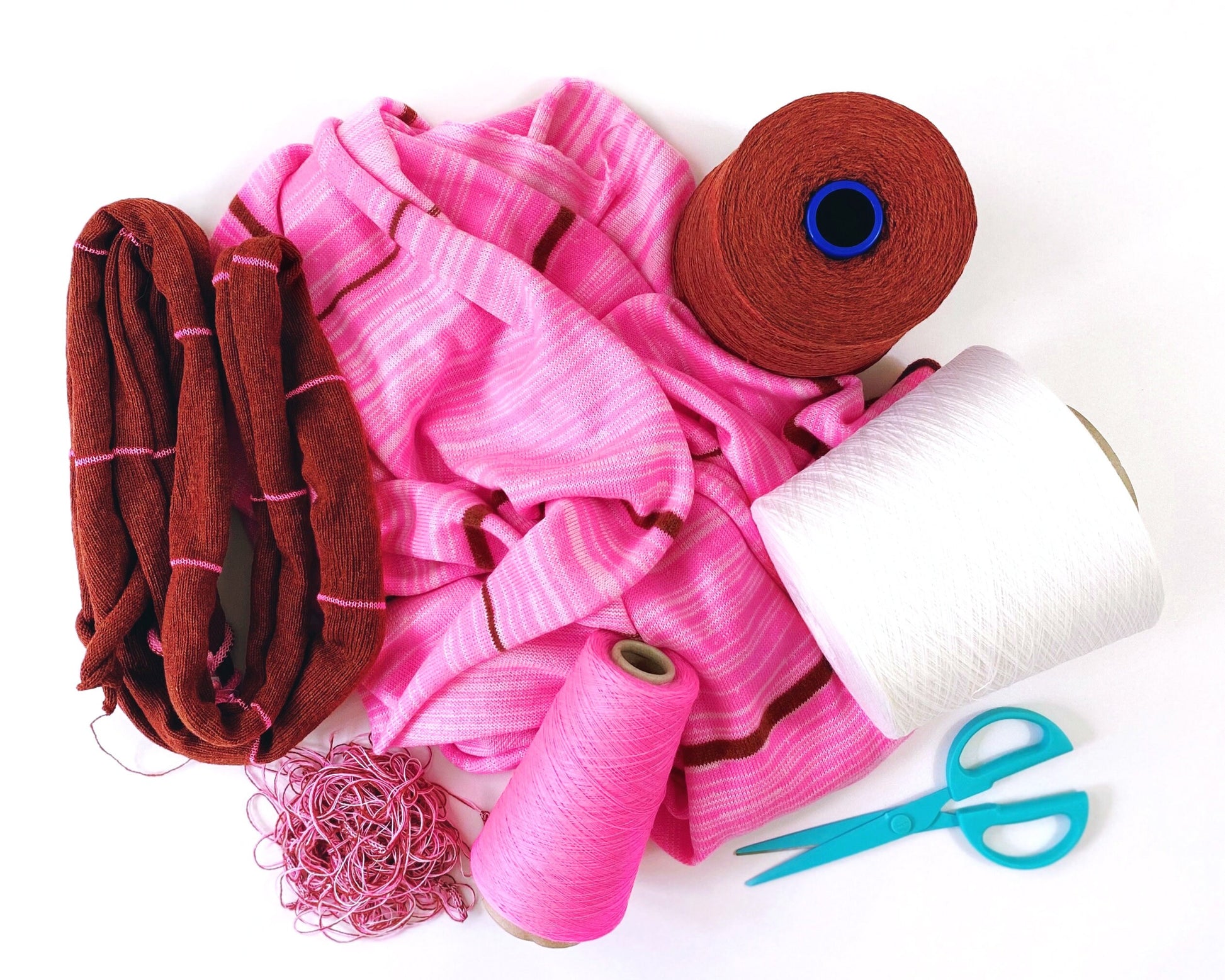 Pink and brown knitted fabric with spools of thread and scissors on a white background