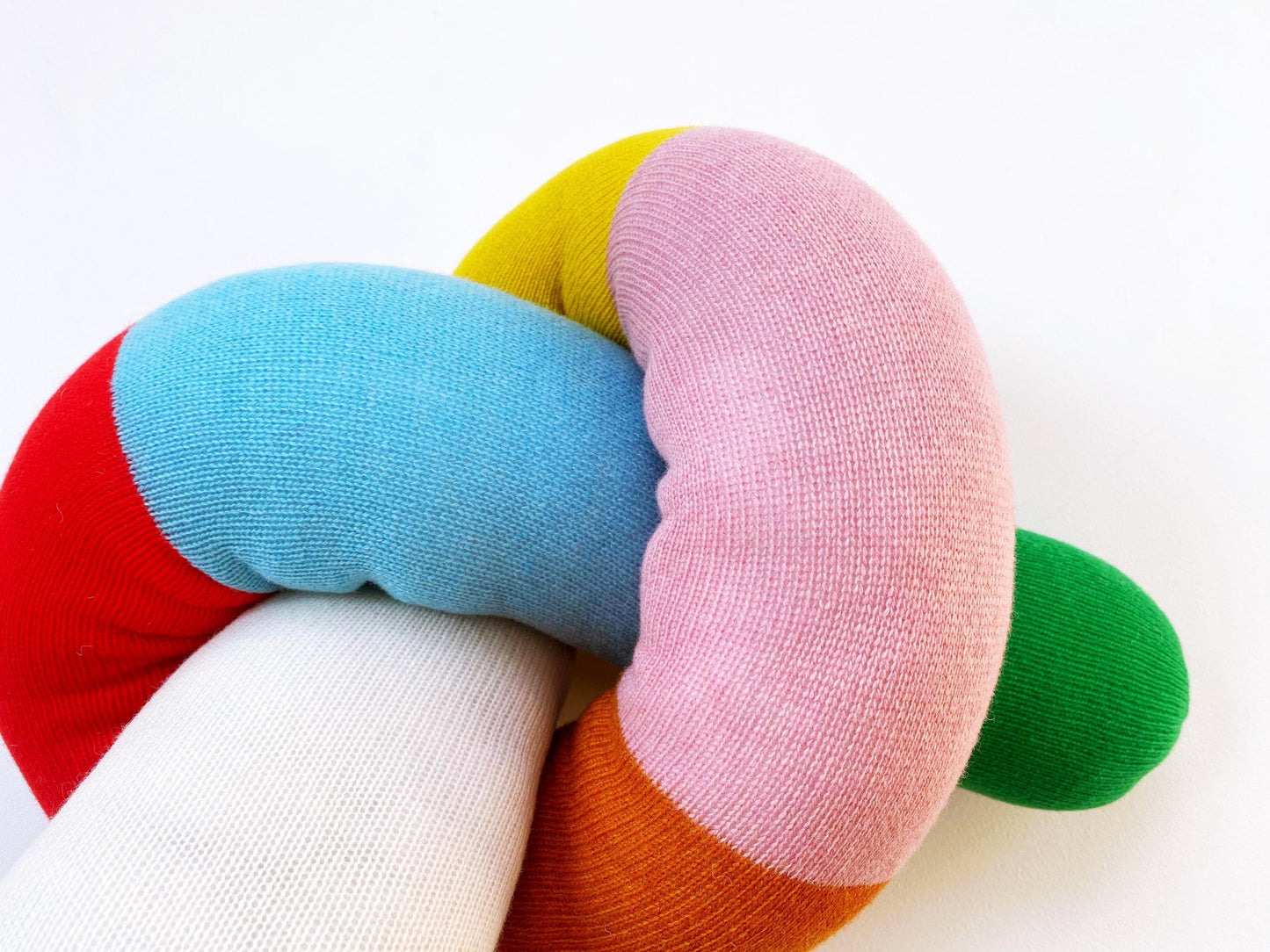 Colorful knitted toy snake with red, blue, yellow, pink, and green sections on a white background