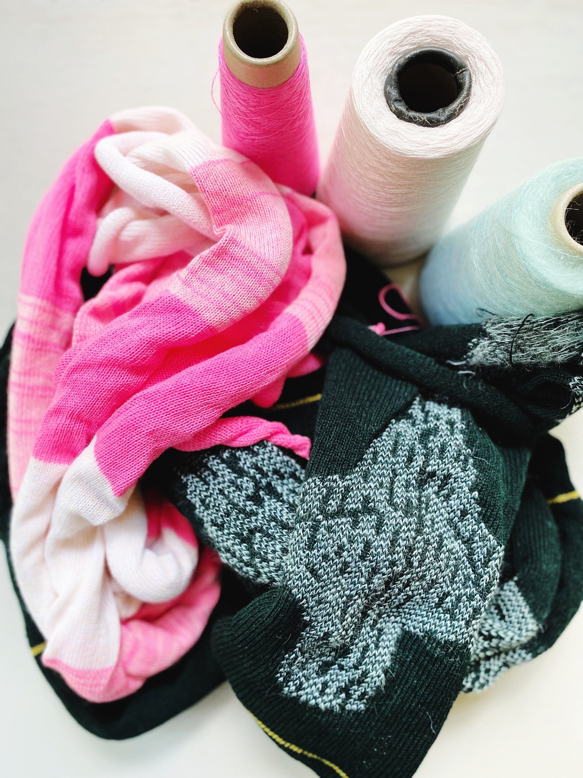 Spools of yarn thread in pink, white, and blue with textured knitted fabrics.