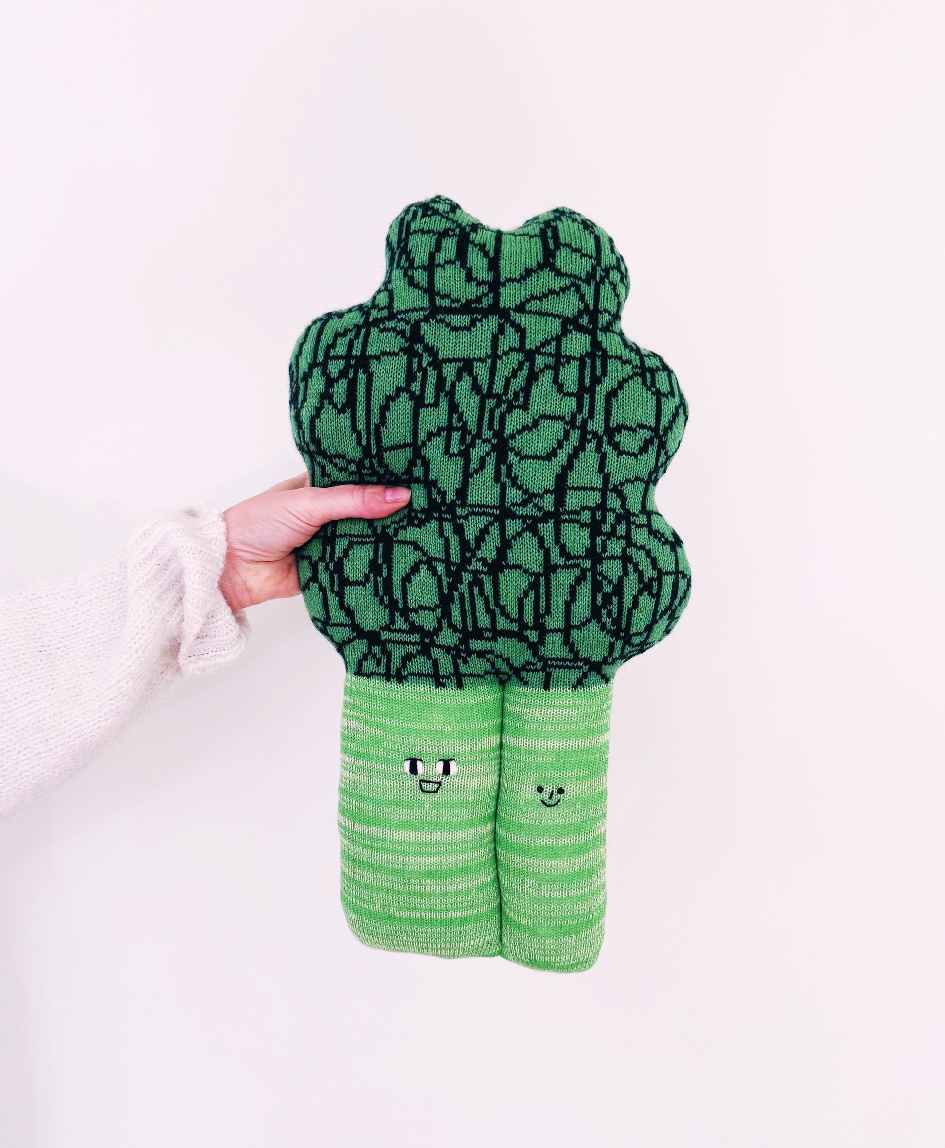 Green plush toy shaped like a broccoli held by a hand on a white background