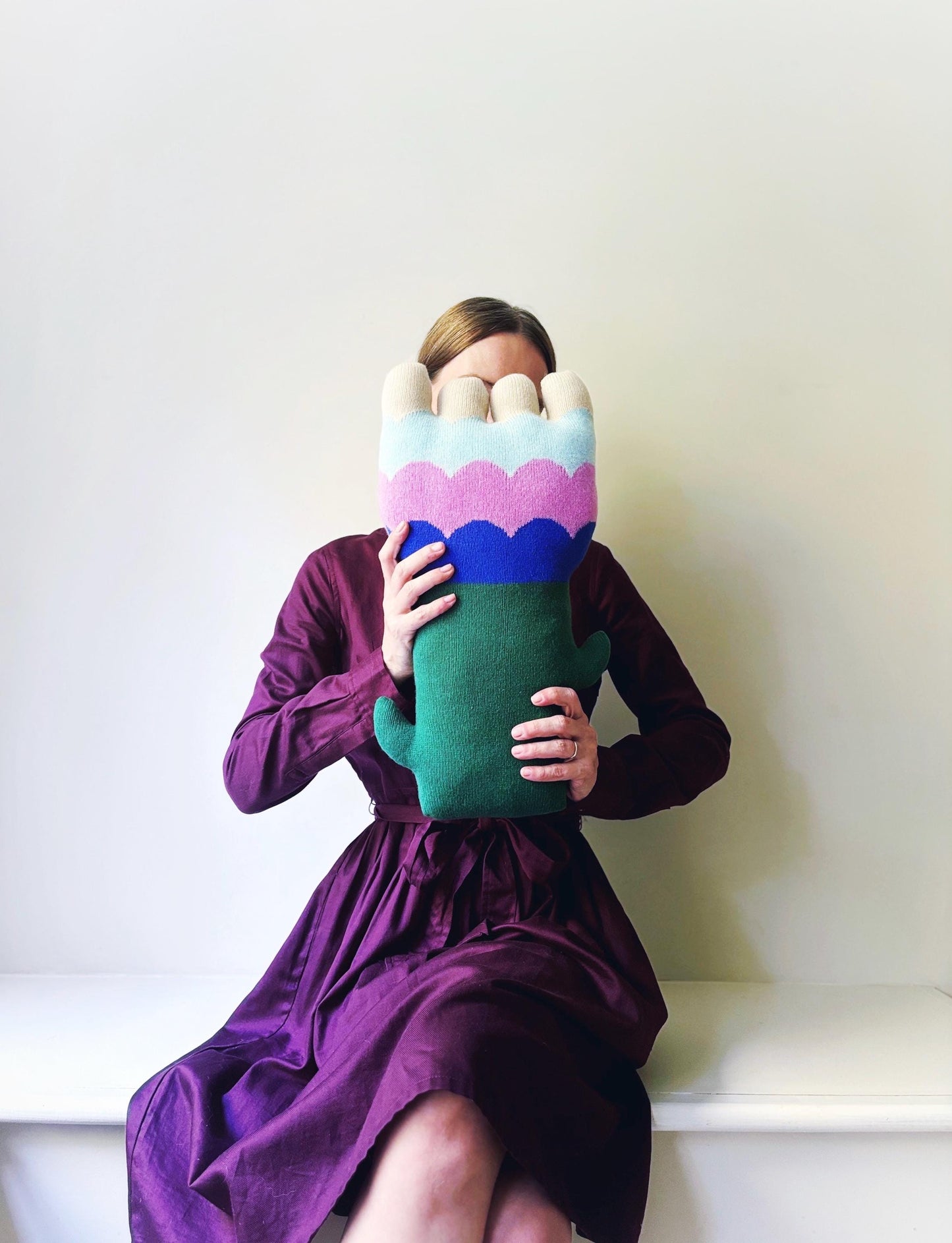 Person holding a colorful flower shaped knitted pillow against a white background