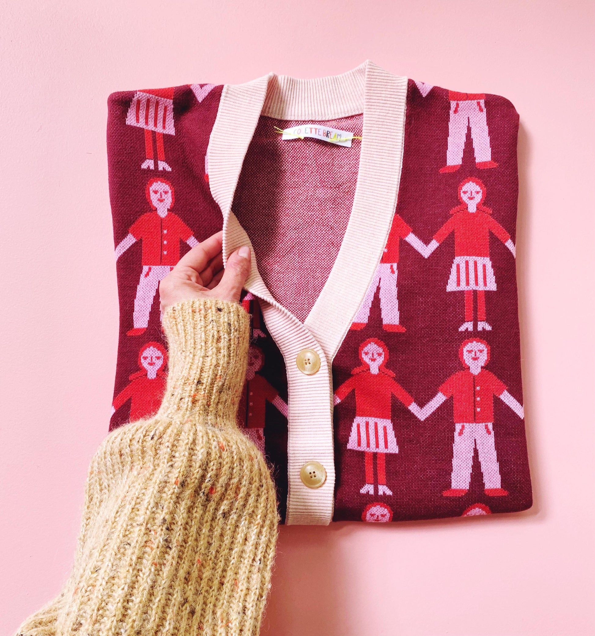 Knitted cardigan with red patterned front held by a hand against a pink background