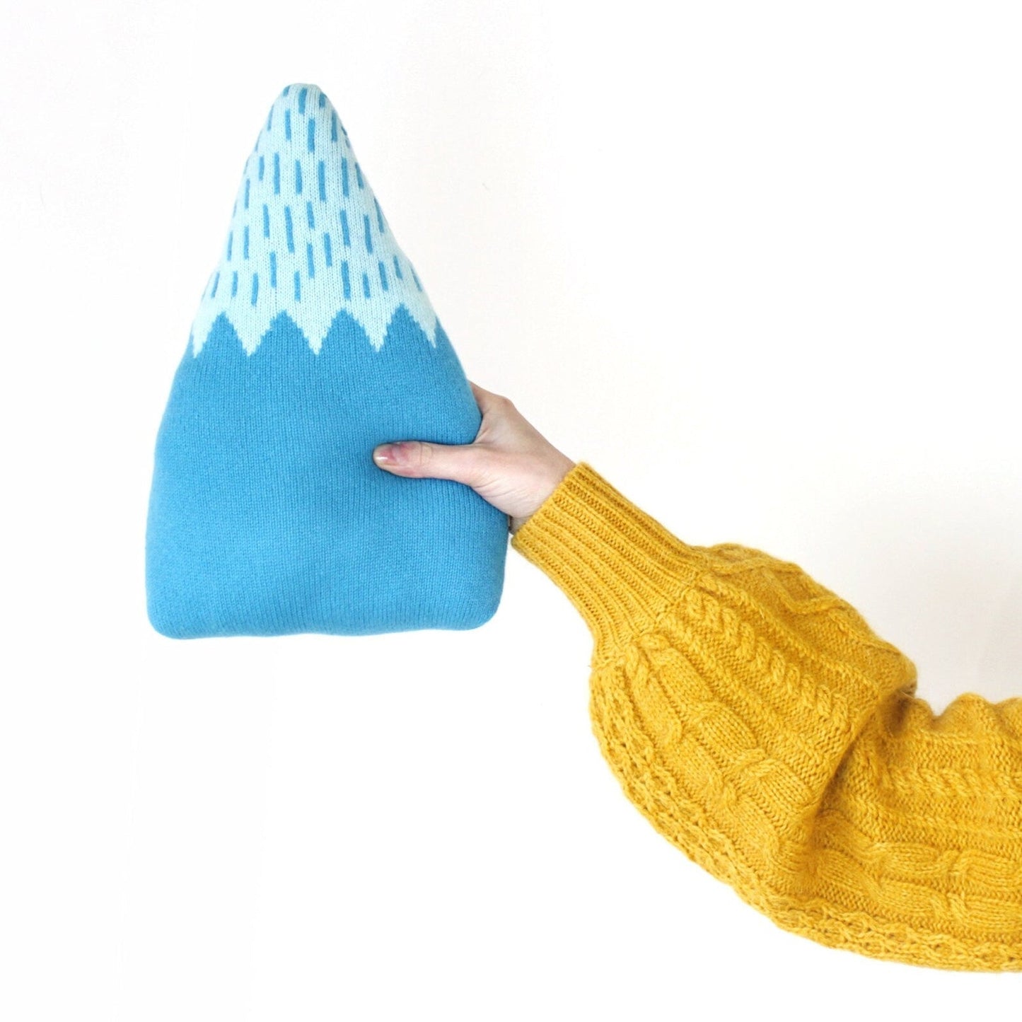 Blue and white patterned mountain shaped pillow held by a person wearing a yellow sweater on a white background