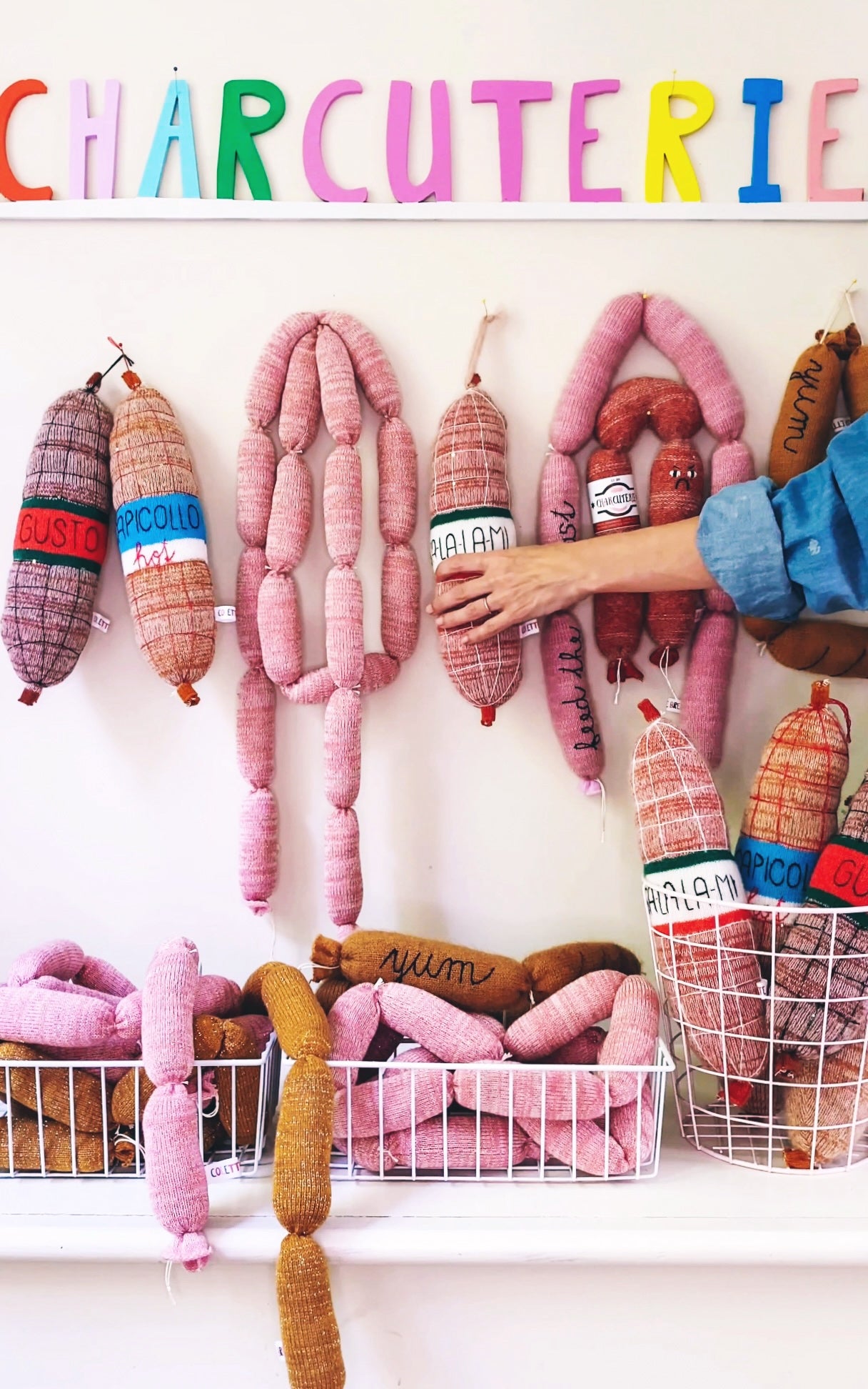 Colorful knitted charcuterie display with various sausage links and a person's hand reaching for one.