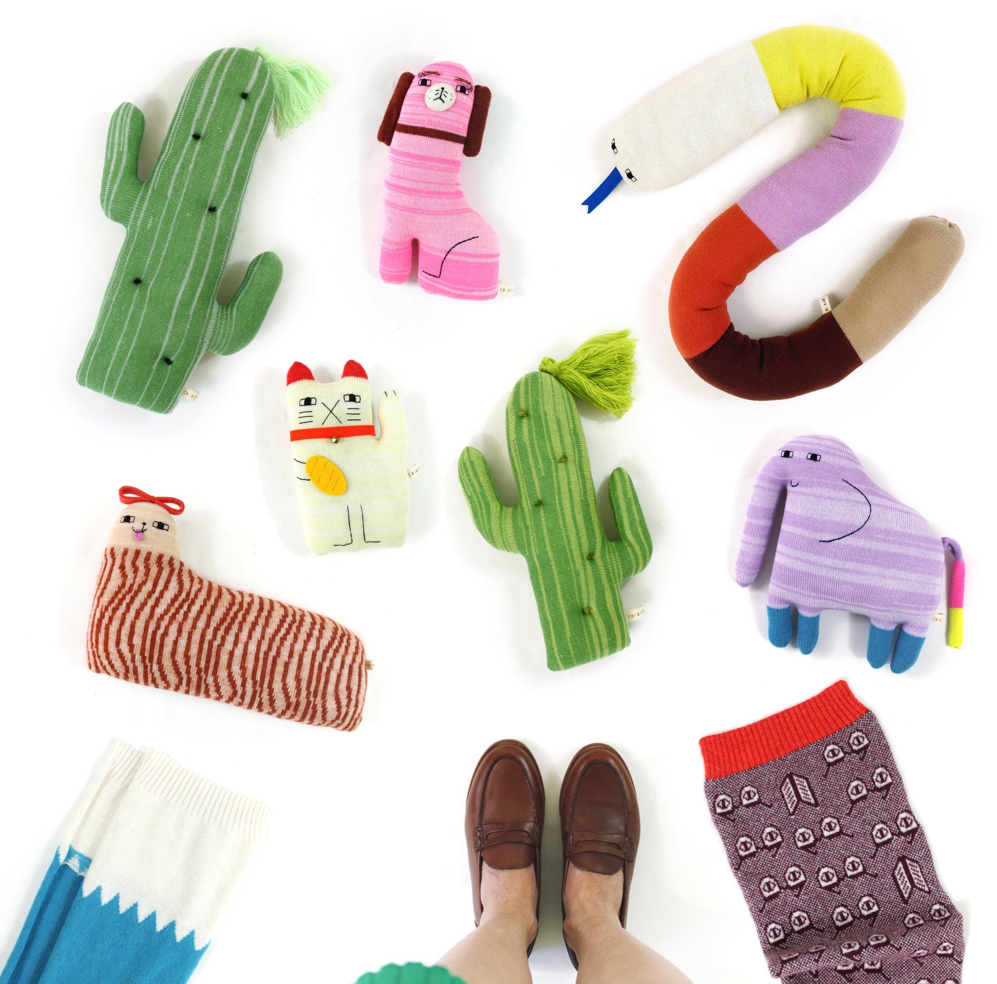 Collection of colorful knitted plush toys and cushions shaped like animals and objects on a white background