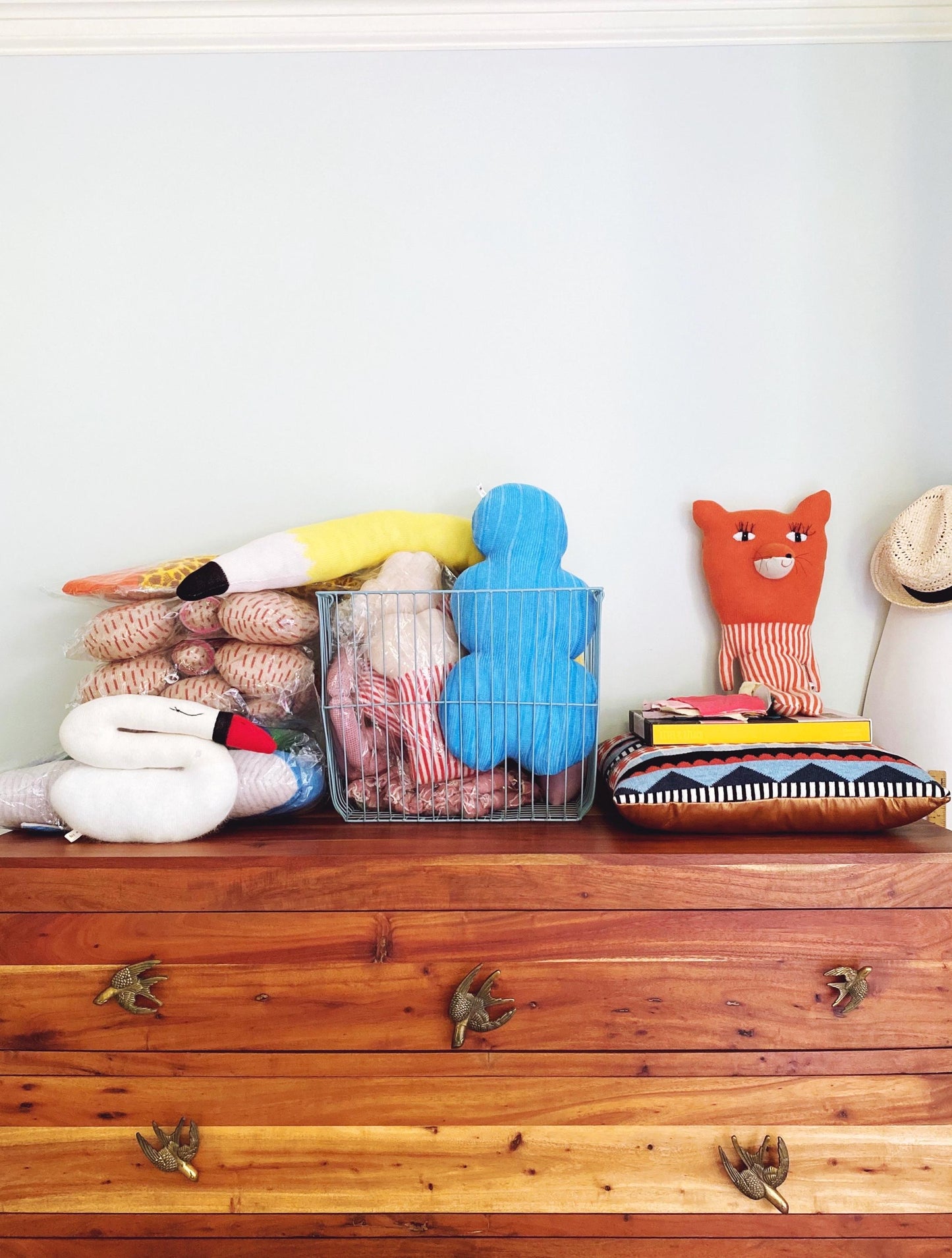 Wooden dresser with various stuffed animals, toys and pillows on top against a white wall.