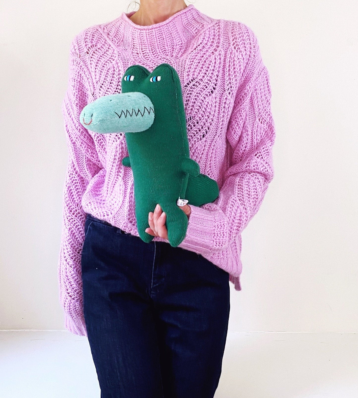Person wearing a pink sweater holding a green knitted crocodile plush toy 
